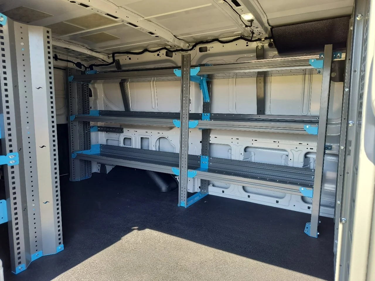 Empty interior of a cargo van with metal shelving units installed on the sides and back.