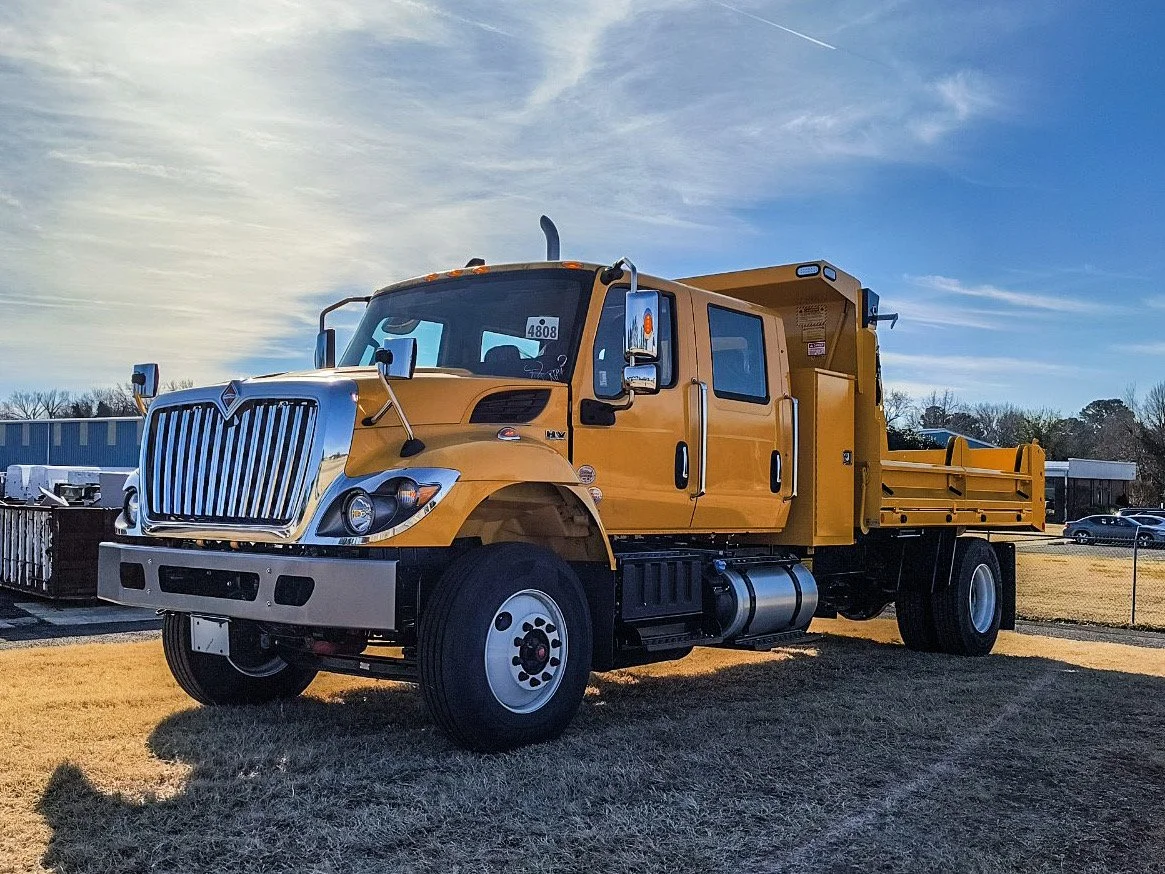Yellow flatbed truck parked on grass field under a partly cloudy sky.