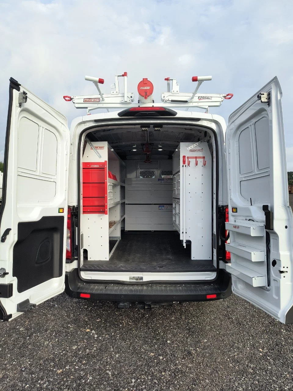 Back of a white utility van with open doors revealing shelves and storage compartments inside. Equipment mounted on the roof.