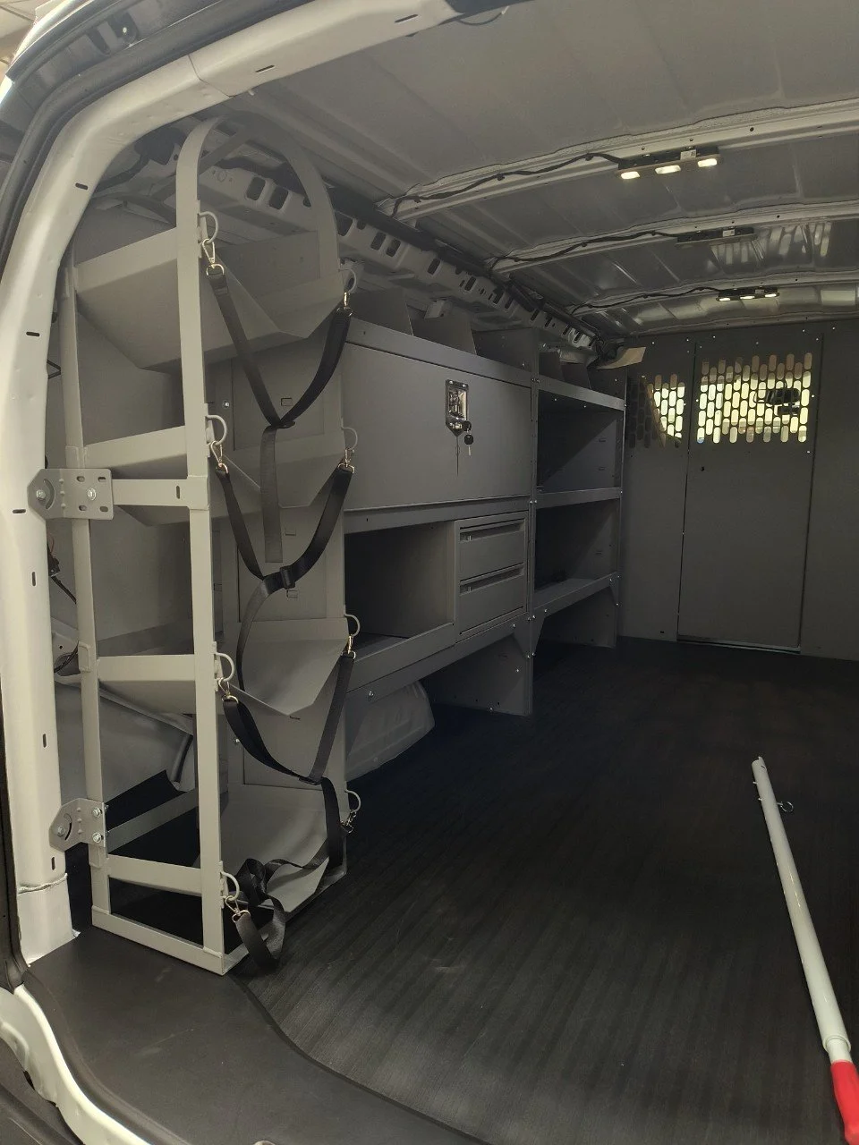Interior of a work van with various storage cabinets, shelves, and straps for securing equipment.