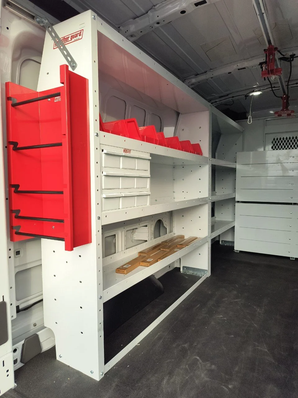 Shelving unit inside a work vehicle with red and white storage bins and compartments.
