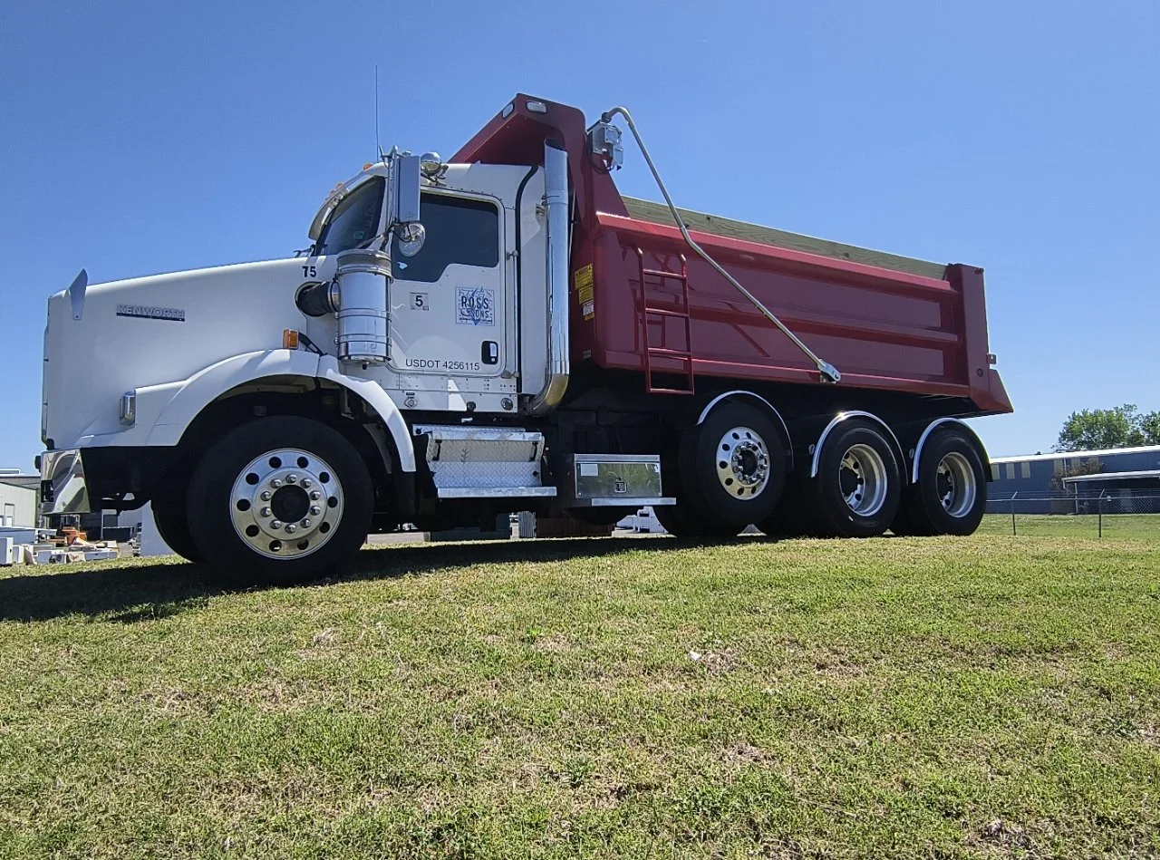 A white and red dump truck parked on grass under a clear blue sky.