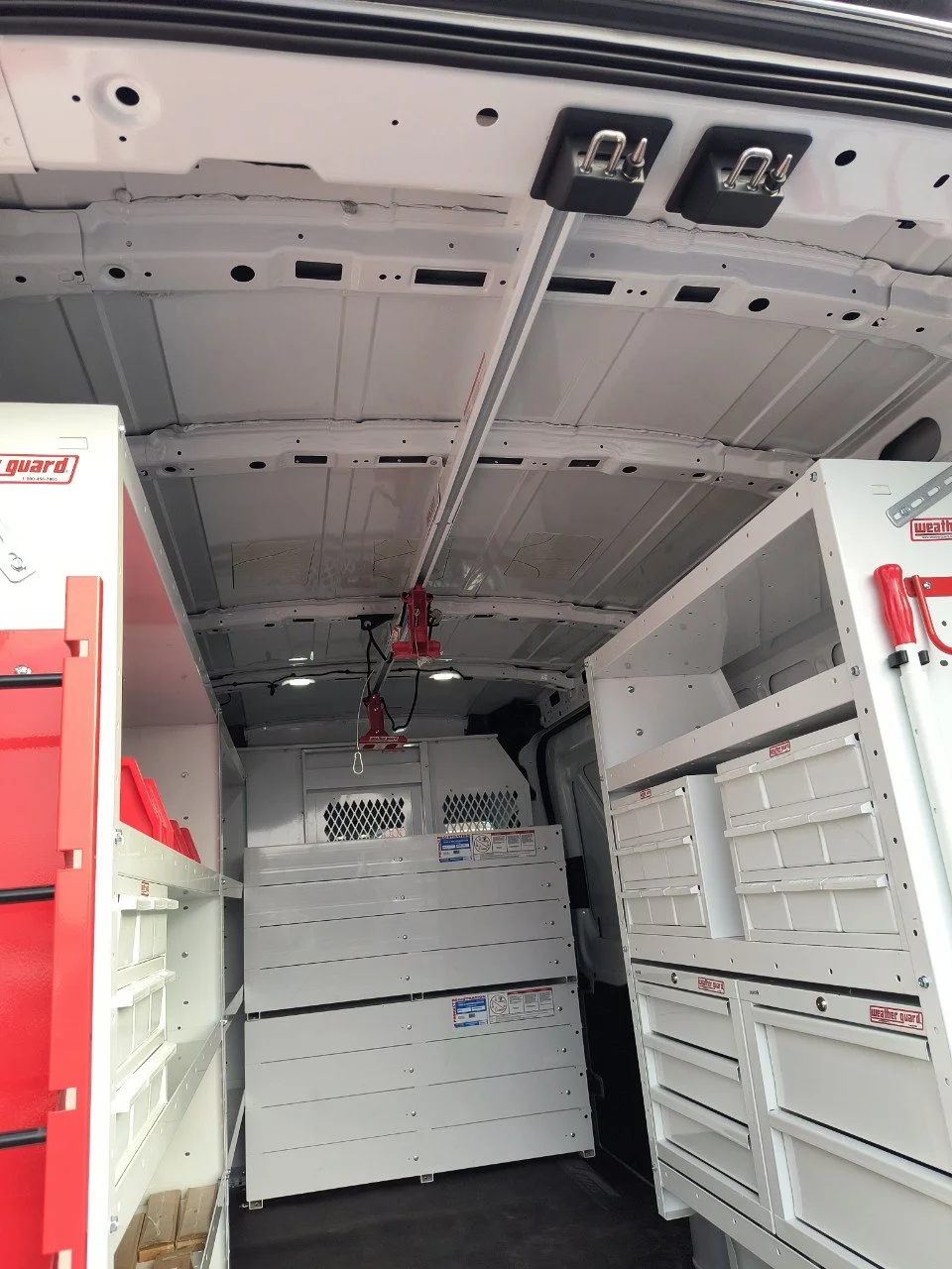 Interior of a utility van with storage cabinets, tools, and a ceiling-mounted lifting device.