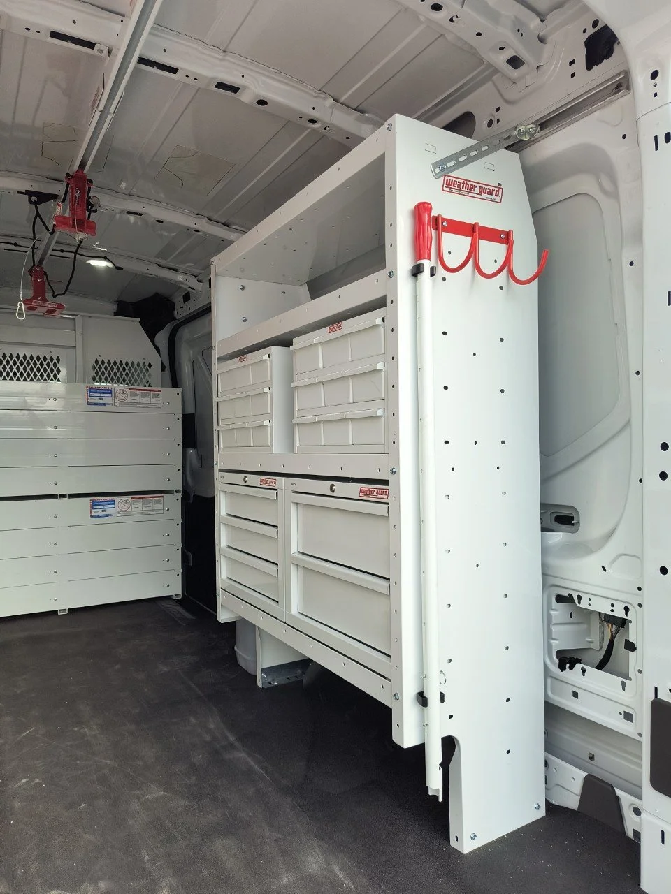 Interior of a utility van with white storage cabinets and red hooks designed for organizing tools.