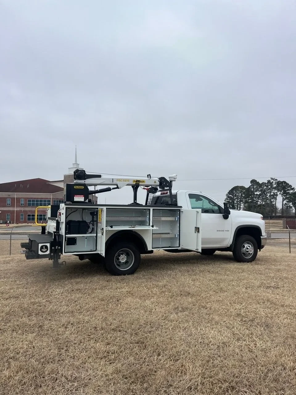 White utility truck with equipment mounted on the back, parked on a grassy field on a cloudy day.