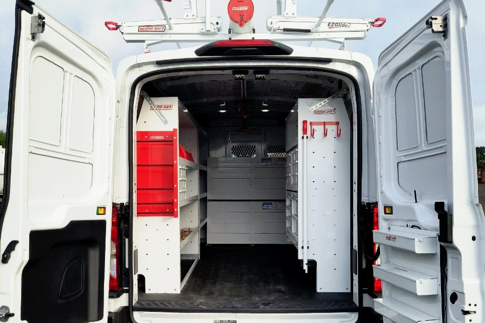 The back of a white utility van with open doors, showing organized storage shelves and hooks inside for tools and equipment.