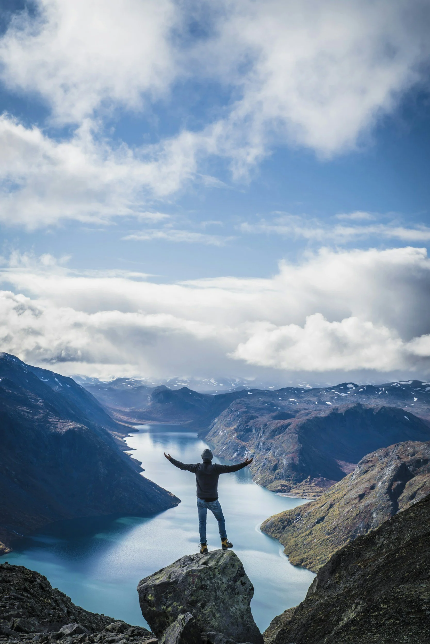 Man on top of mountain looking down into a river valley with his arms outstretched