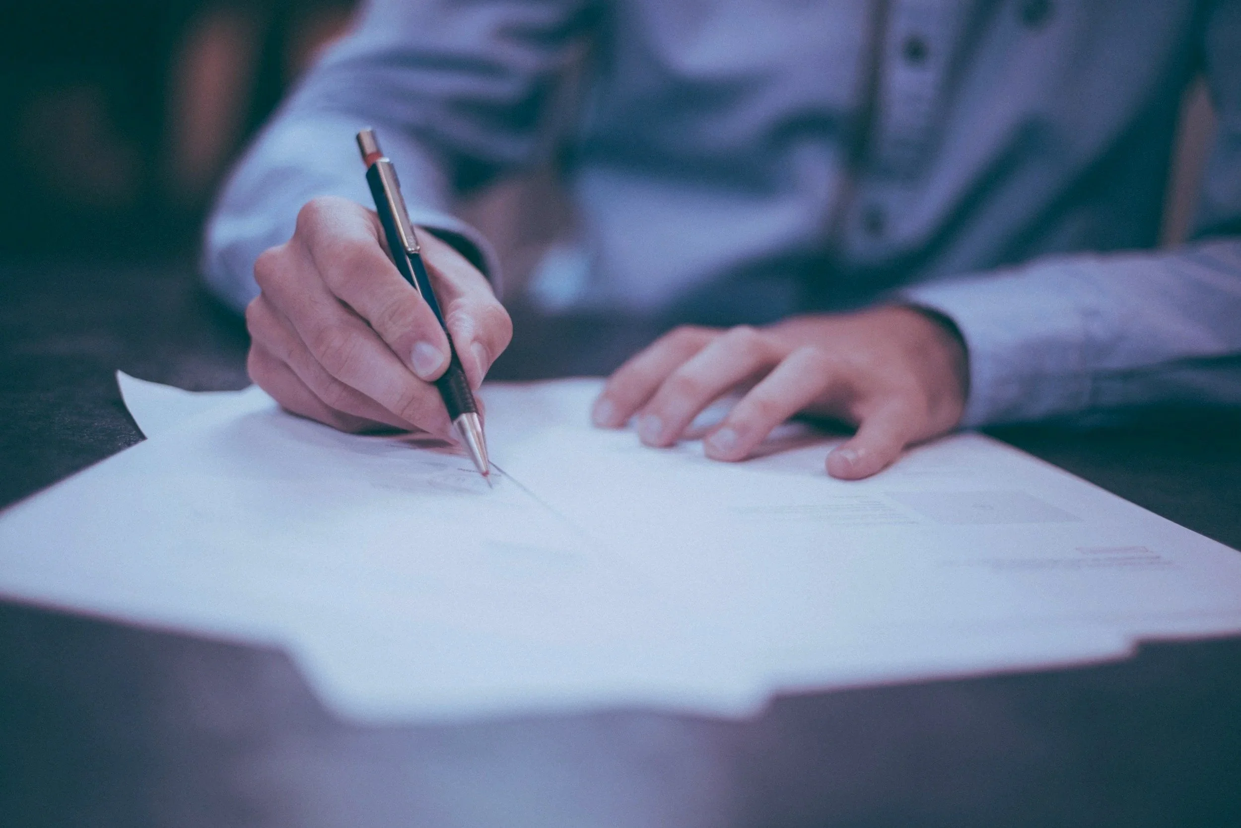 Close-up of a person writing on white paper with a black ballpoint pen.