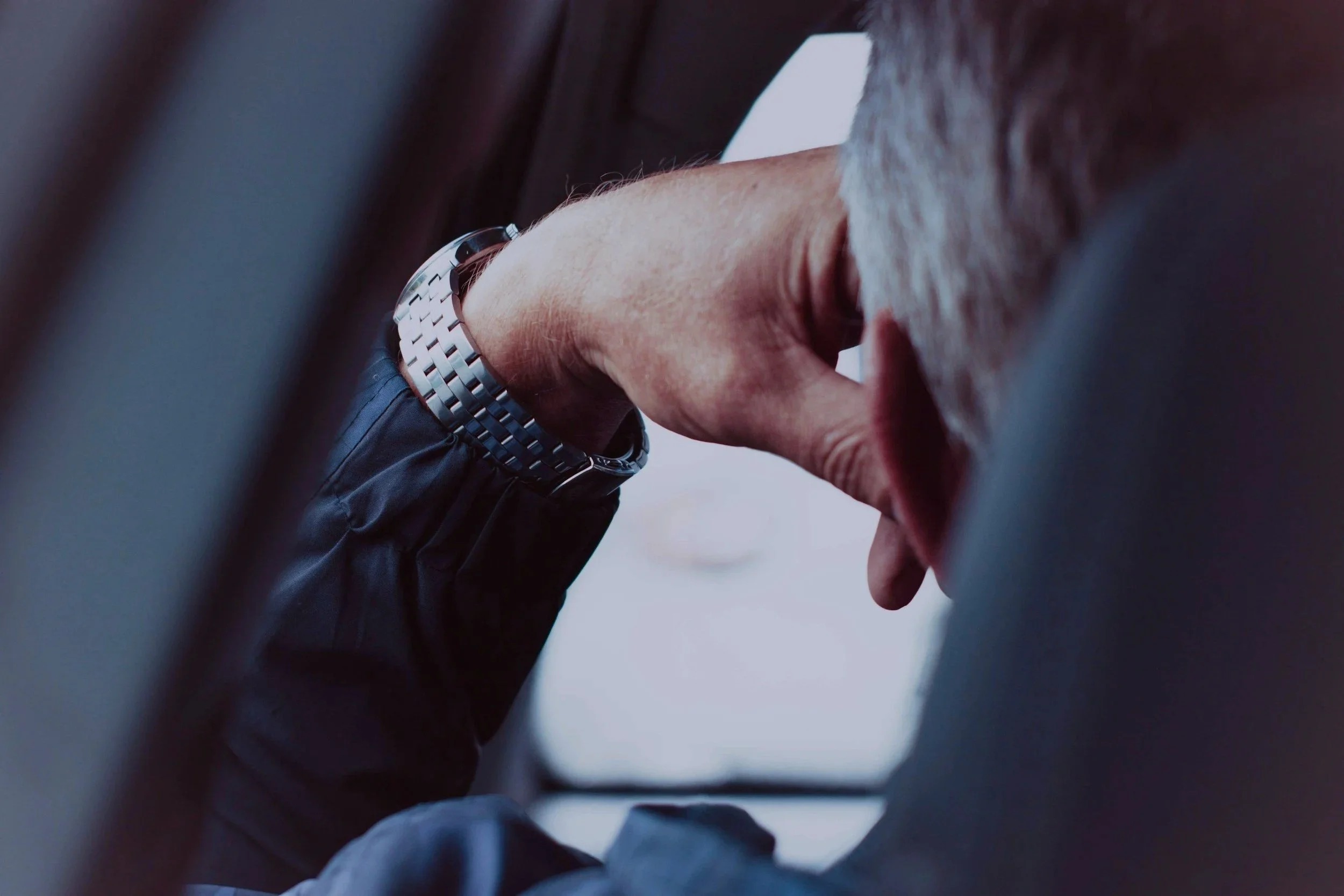 Close-up of a person's hand with a silver watch, seen from above, with grey hair partially visible, reaching out inside a dark enclosed space.