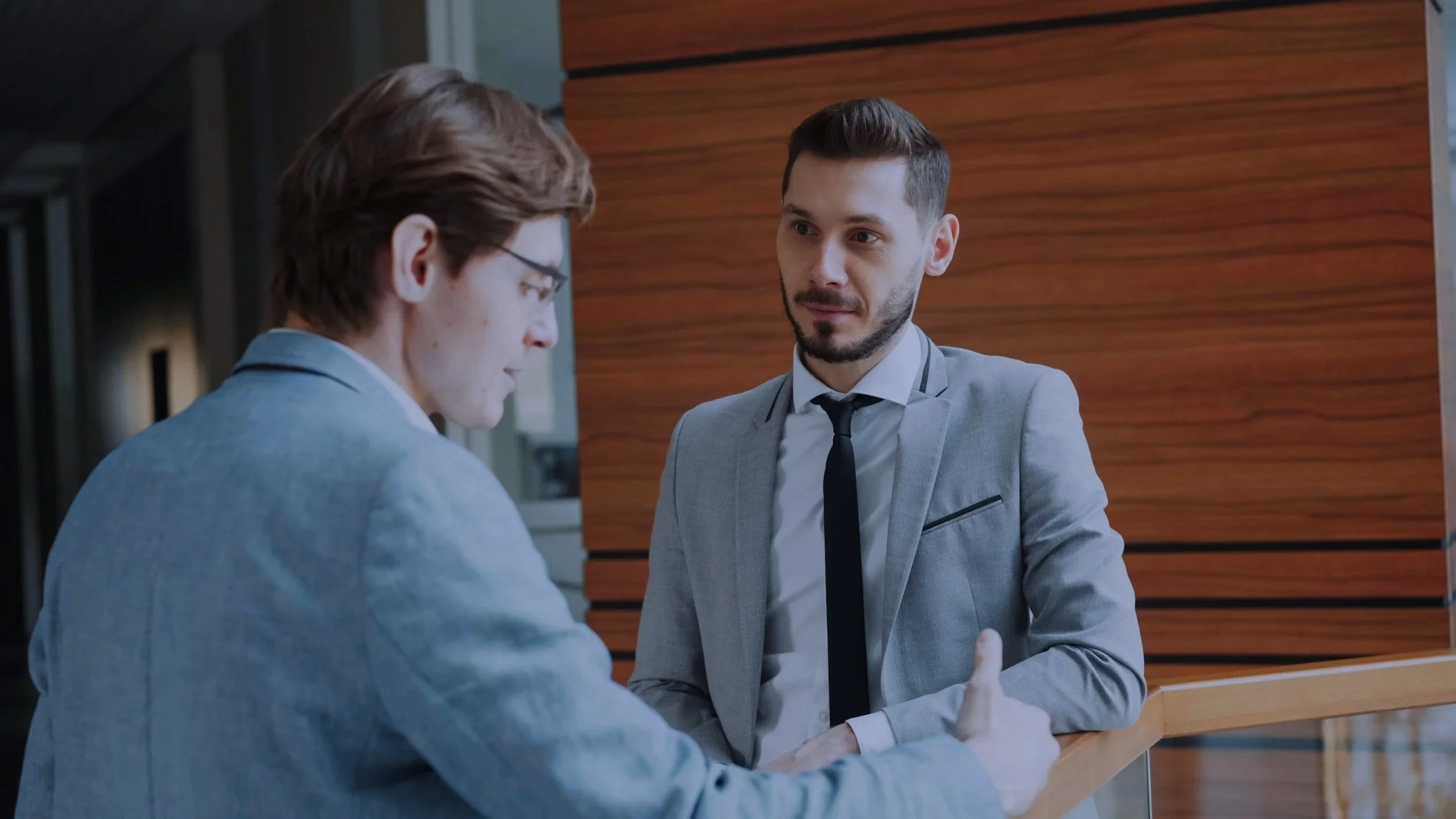 Two men in suits having a conversation at a reception desk in a modern office building.