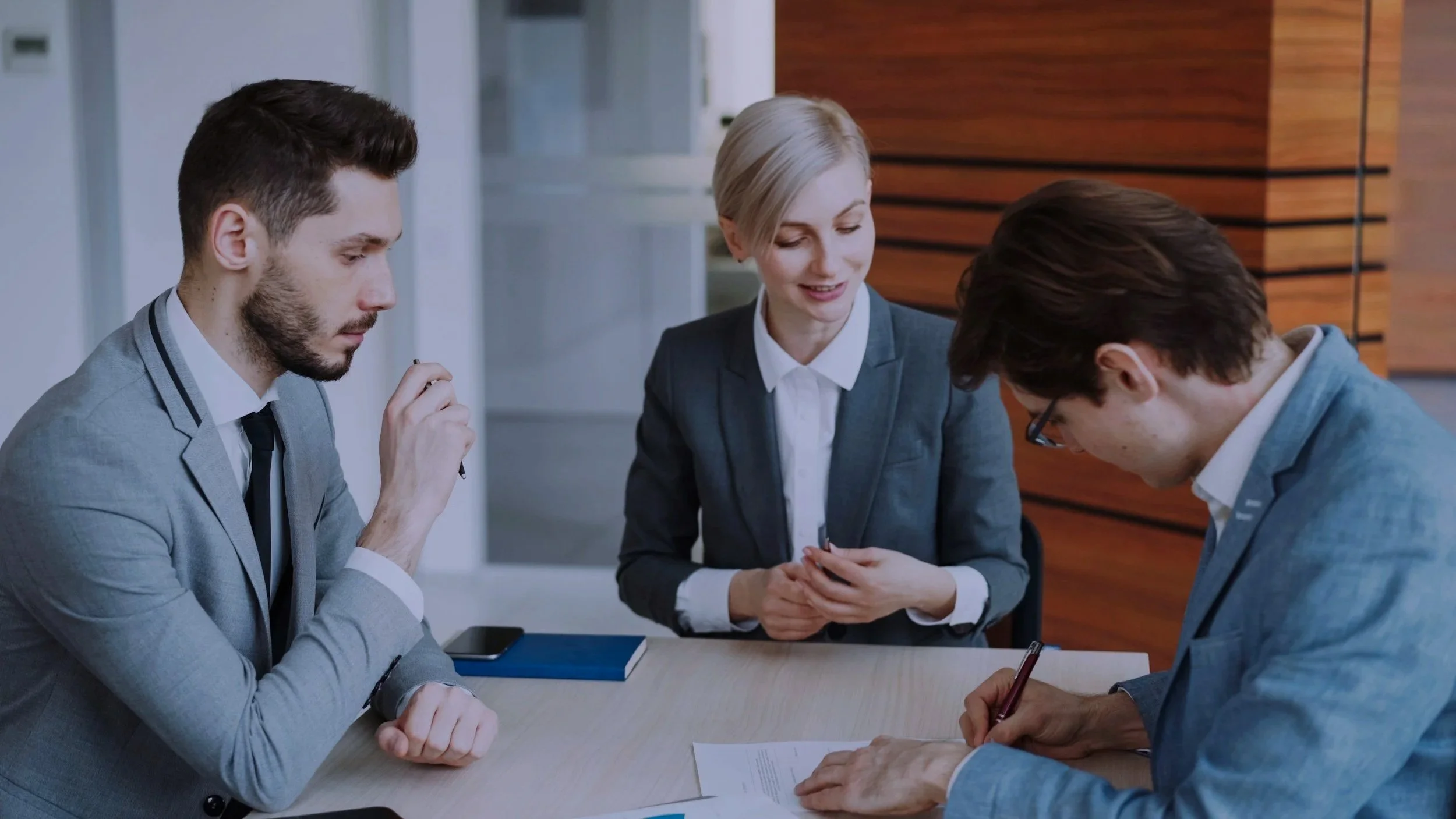 Four business professionals, two men and two women, engaged in a discussion at a meeting table in an office setting.