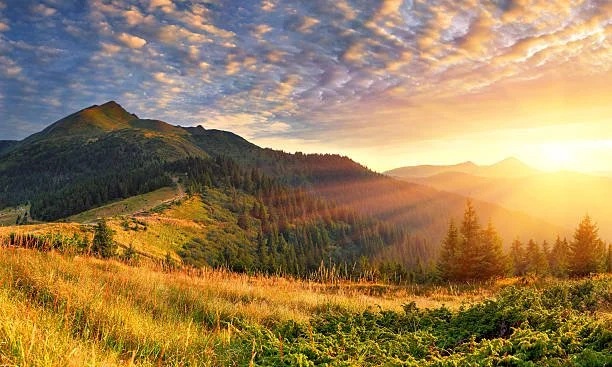 Sunset over a mountain landscape with green hills and trees, partly cloudy sky.