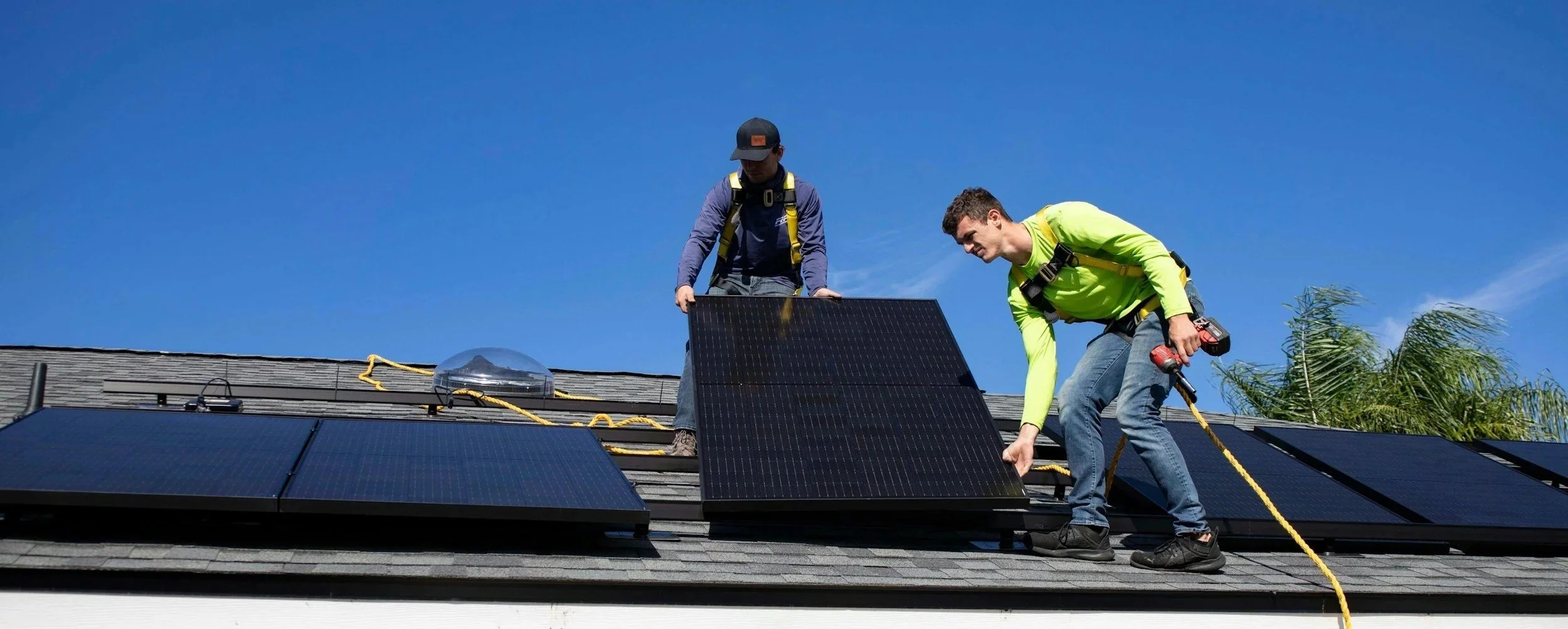 Two workers installing solar panels on a house roof on a clear day.