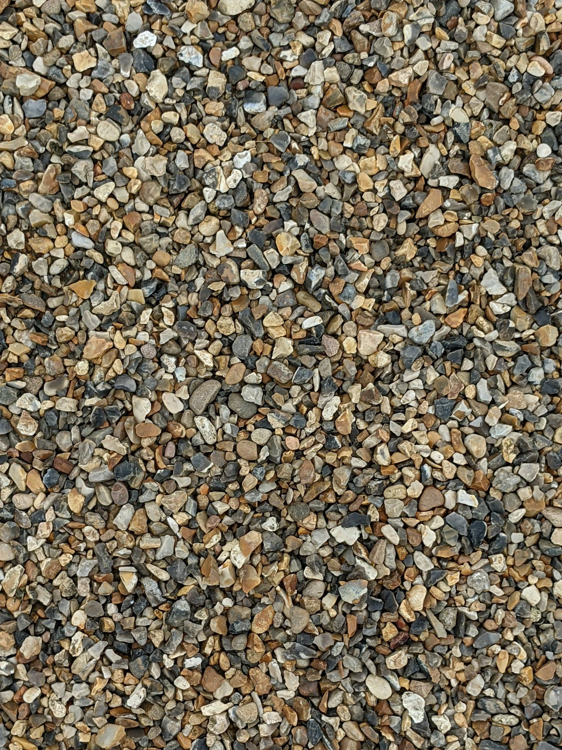 Close-up view of small, multicolored gravel stones covering the ground, with shades of brown, gray, black, and beige.