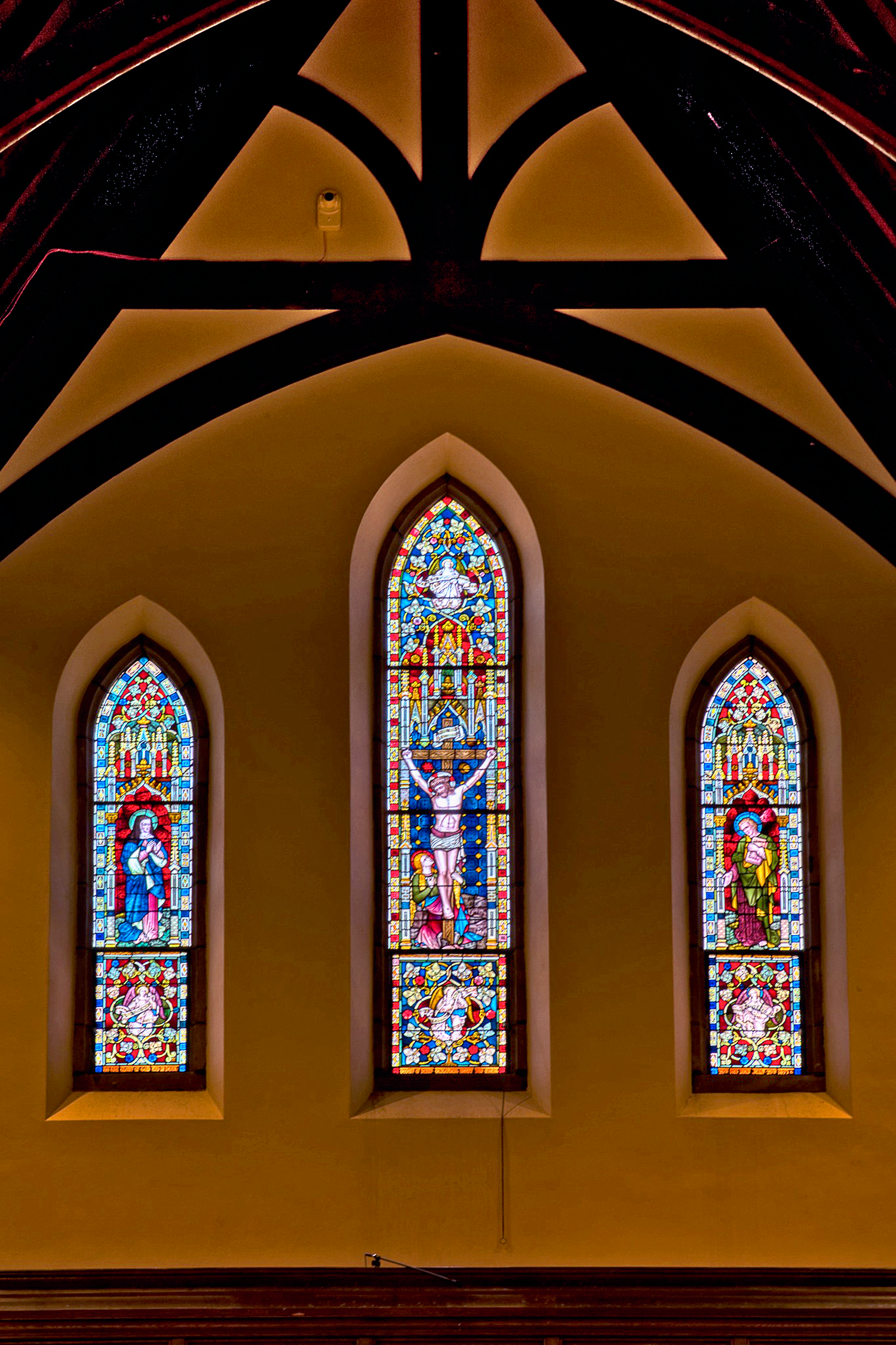Three vertical stained glass windows and a high vaulted ceiling inside St. Thomas’ Church Whitemarsh.
