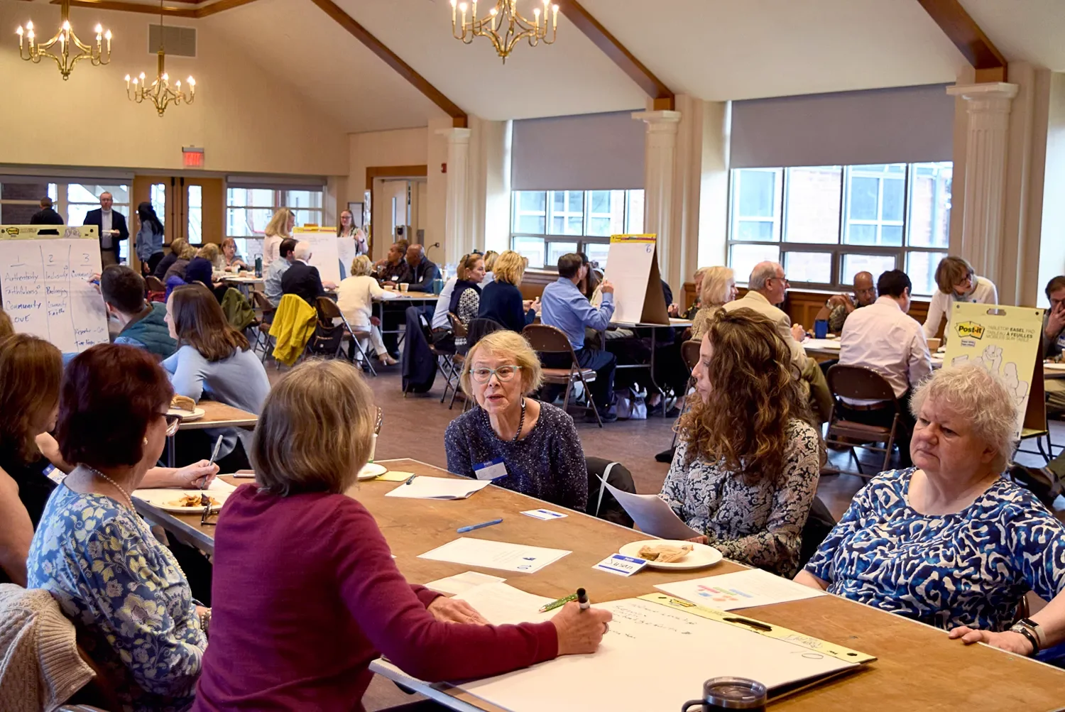 Small groups of people working together at long tables in a large room at a workshop at St. Thomas’ Church Whitemarsh.