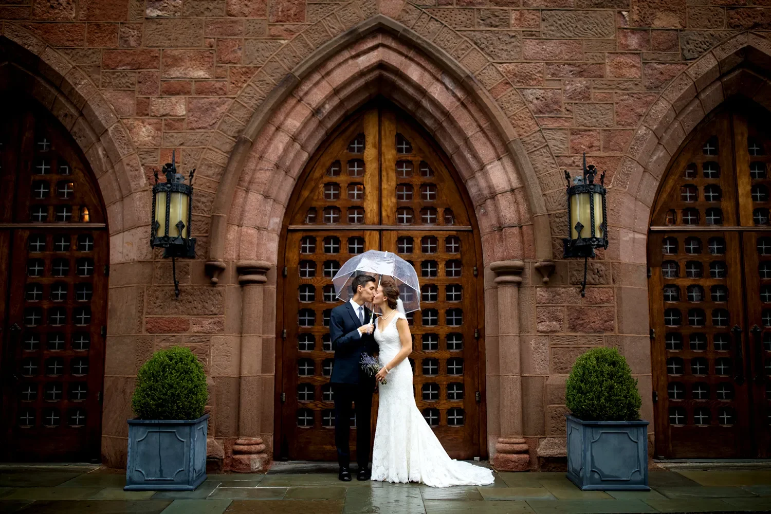 Bride and groom kissing under umbrella in front of main church doors at The Retreat at St. Thomas’ Church Whitemarsh.