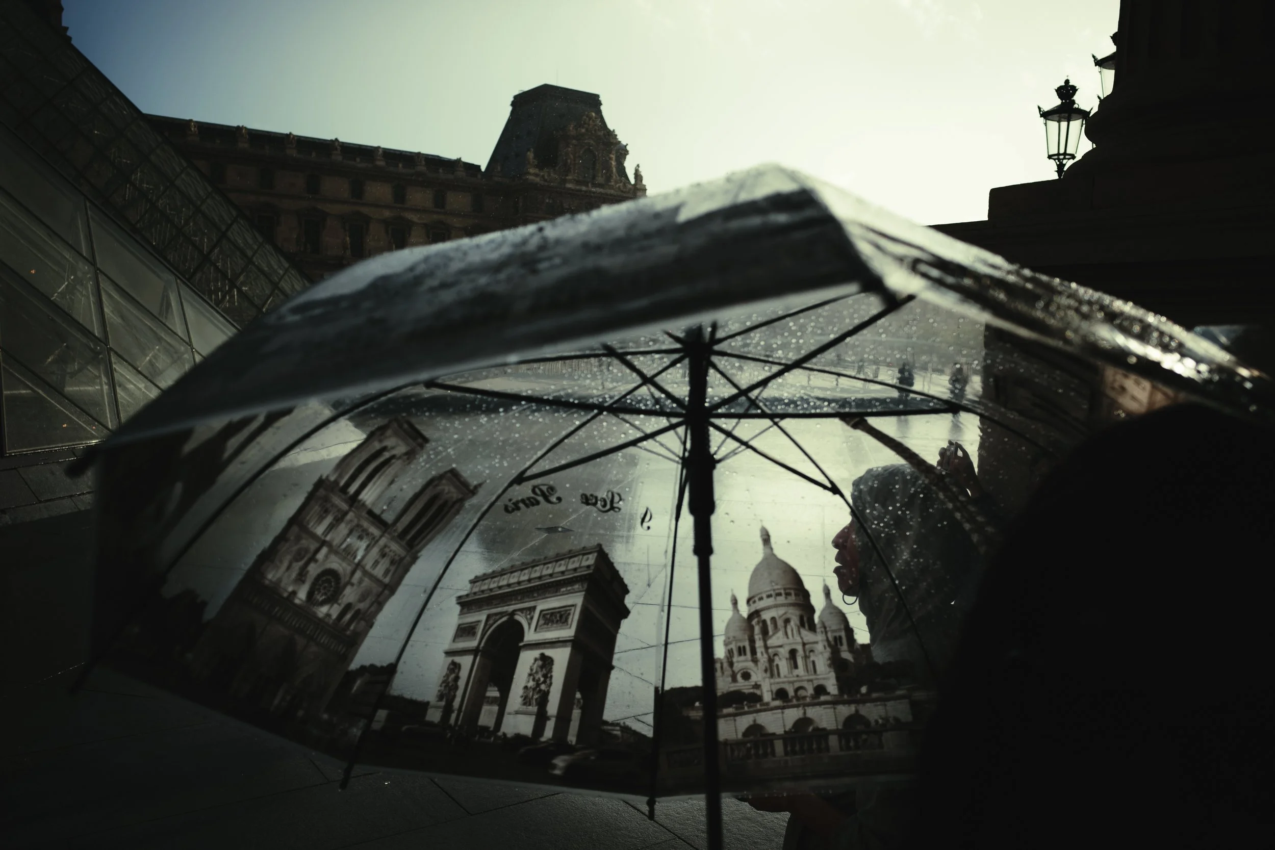 An umbrella with raindrops, reflecting buildings and a dome from a cityscape under a cloudy sky.