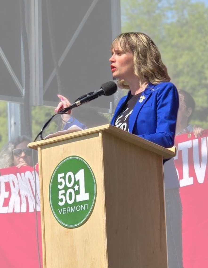 A photo of Tanya standing on a stage behind a lecturn speaking into a microphone
