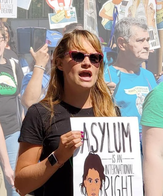 A photo of Tanya in a crowd of protesters holding a sign that says Asylum is an International Right
