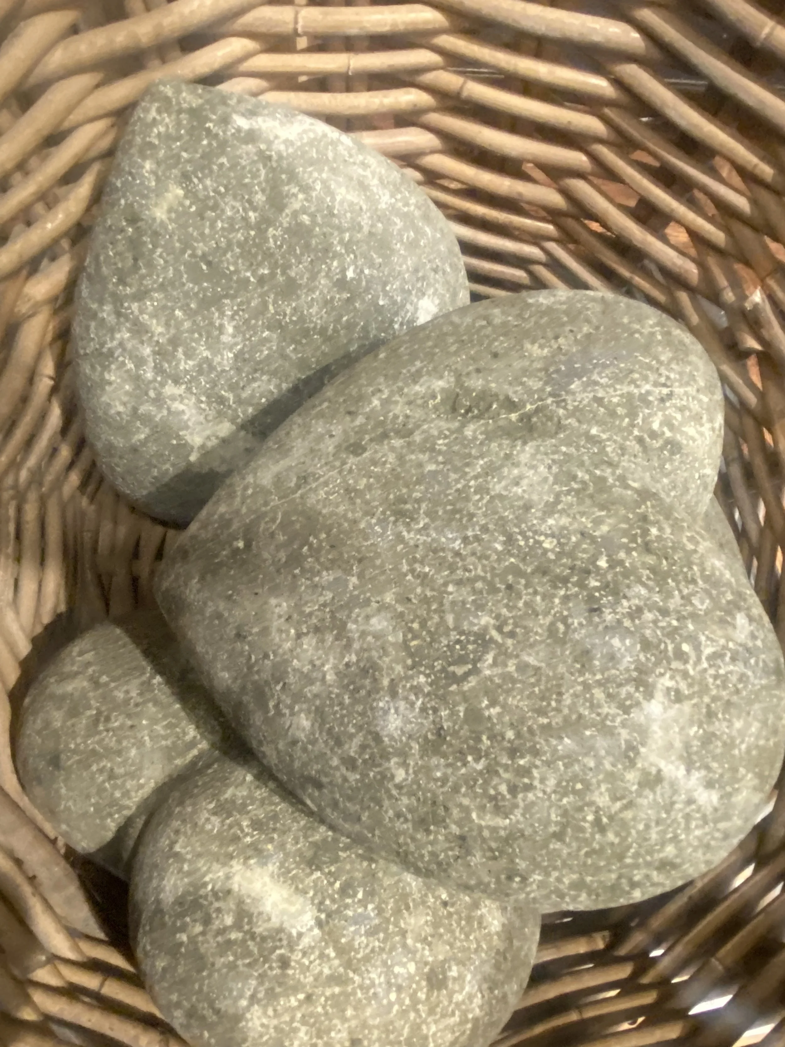 Close-up of three smooth, rounded gray stones in a woven wicker basket.