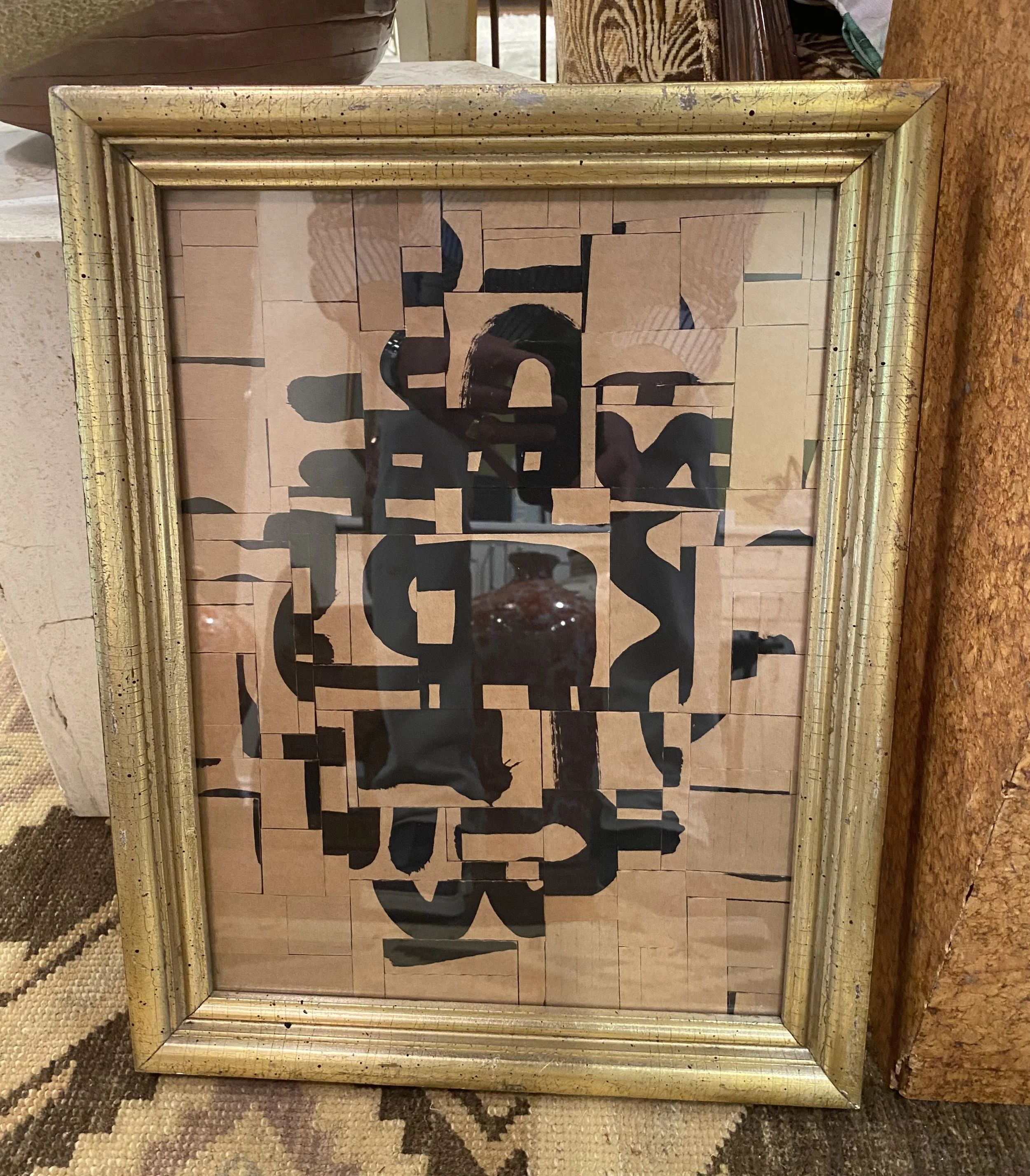 A mirror with a gold frame reflecting a lion-shaped artwork made of wooden and black pieces, placed on a marble surface with a textured rug underneath.