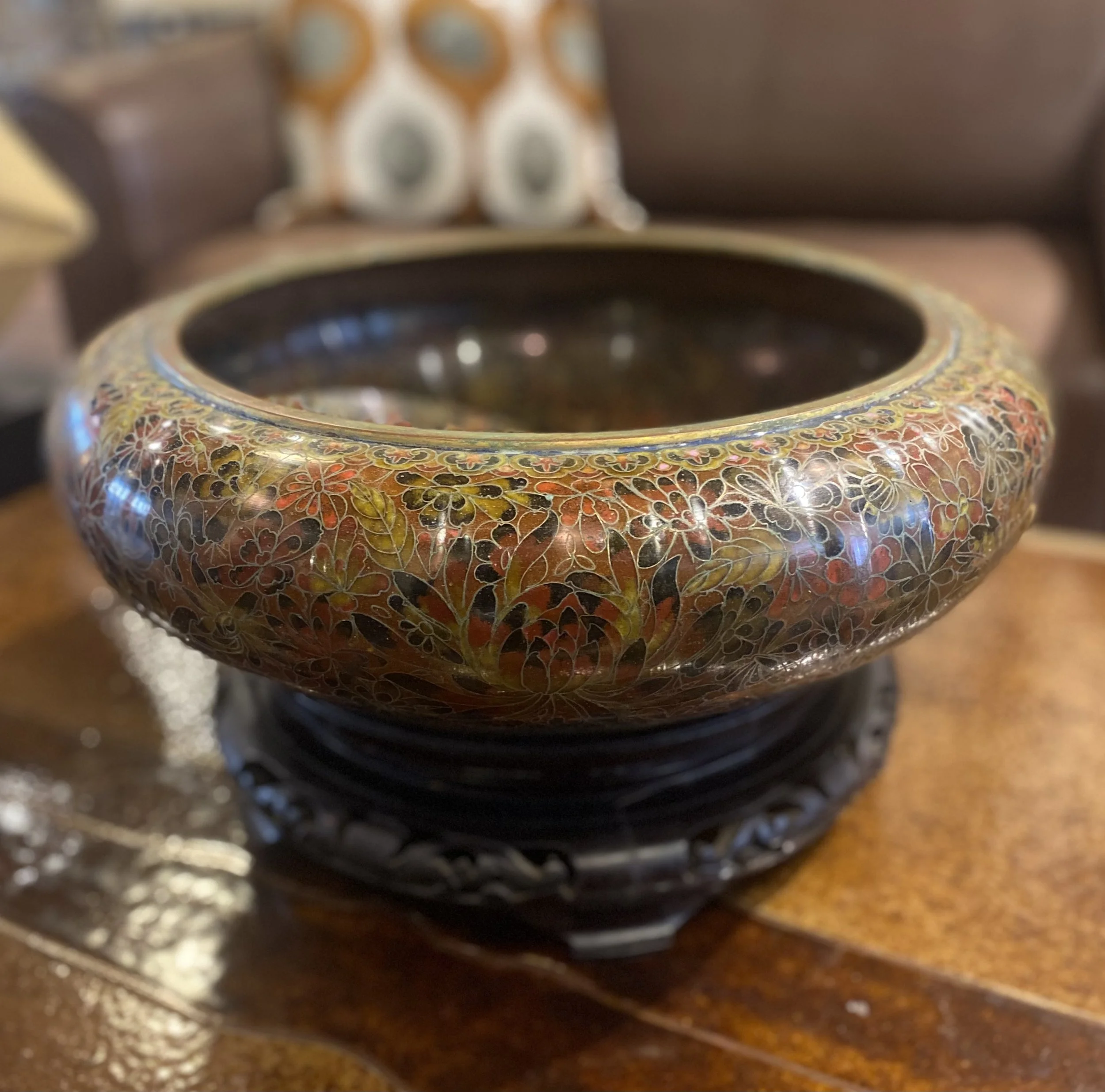 Close-up of an ornate, decorative bowl with an intricate floral pattern, placed on a wooden surface with other similar items in the background.