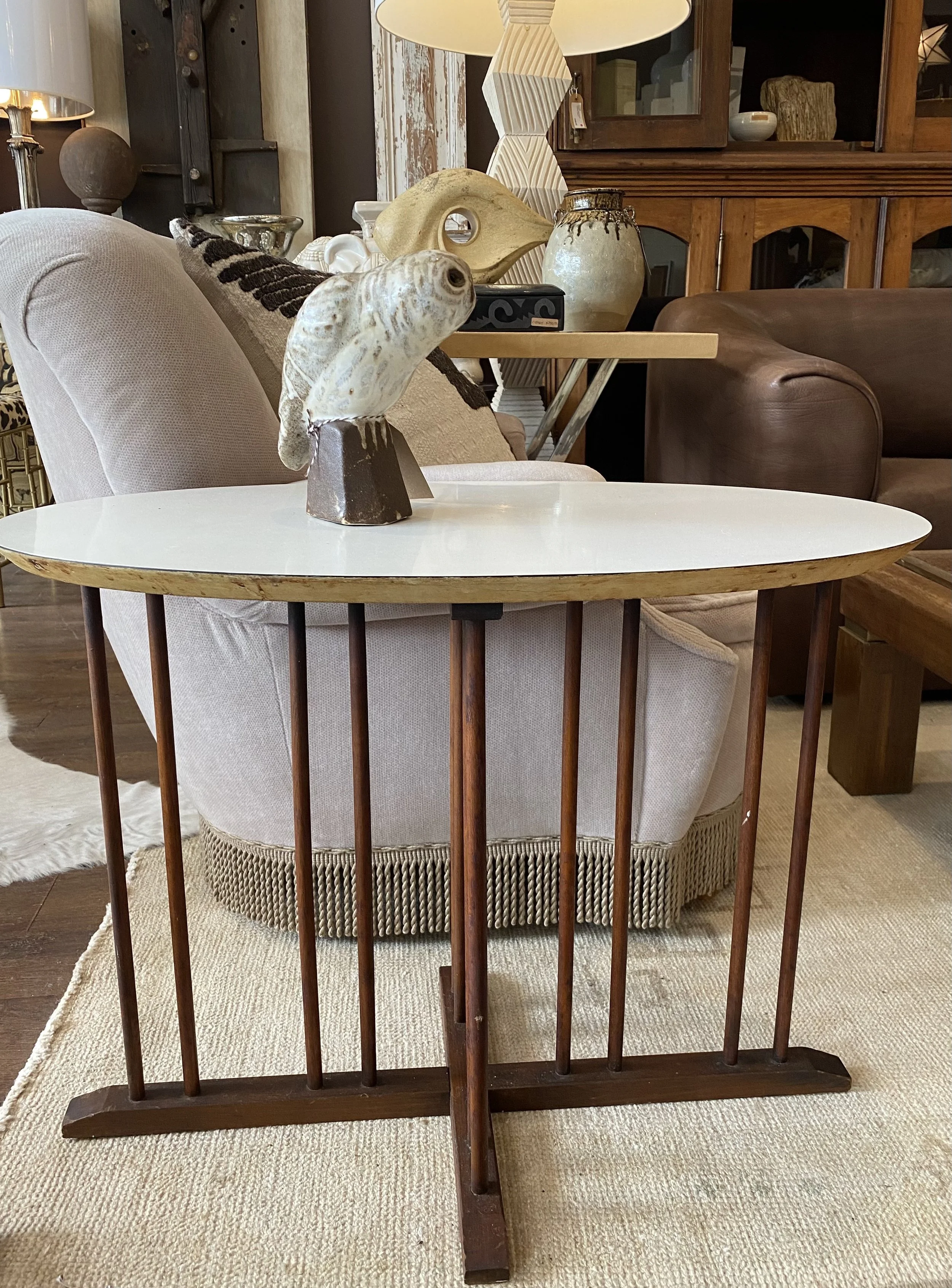 A living room with a beige sofa, a wooden railing, and a side table with decorative items including a fish sculpture and vases. In the background, there is a wooden cabinet and various decorative objects on top.