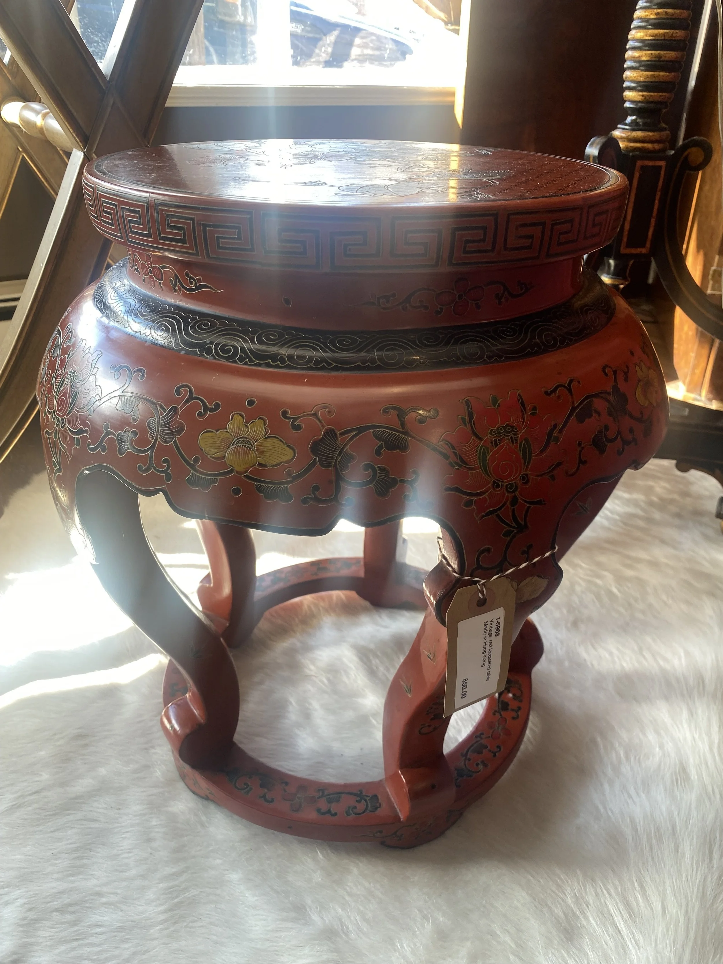 A decorative wooden stool with red and black floral and geometric patterns.