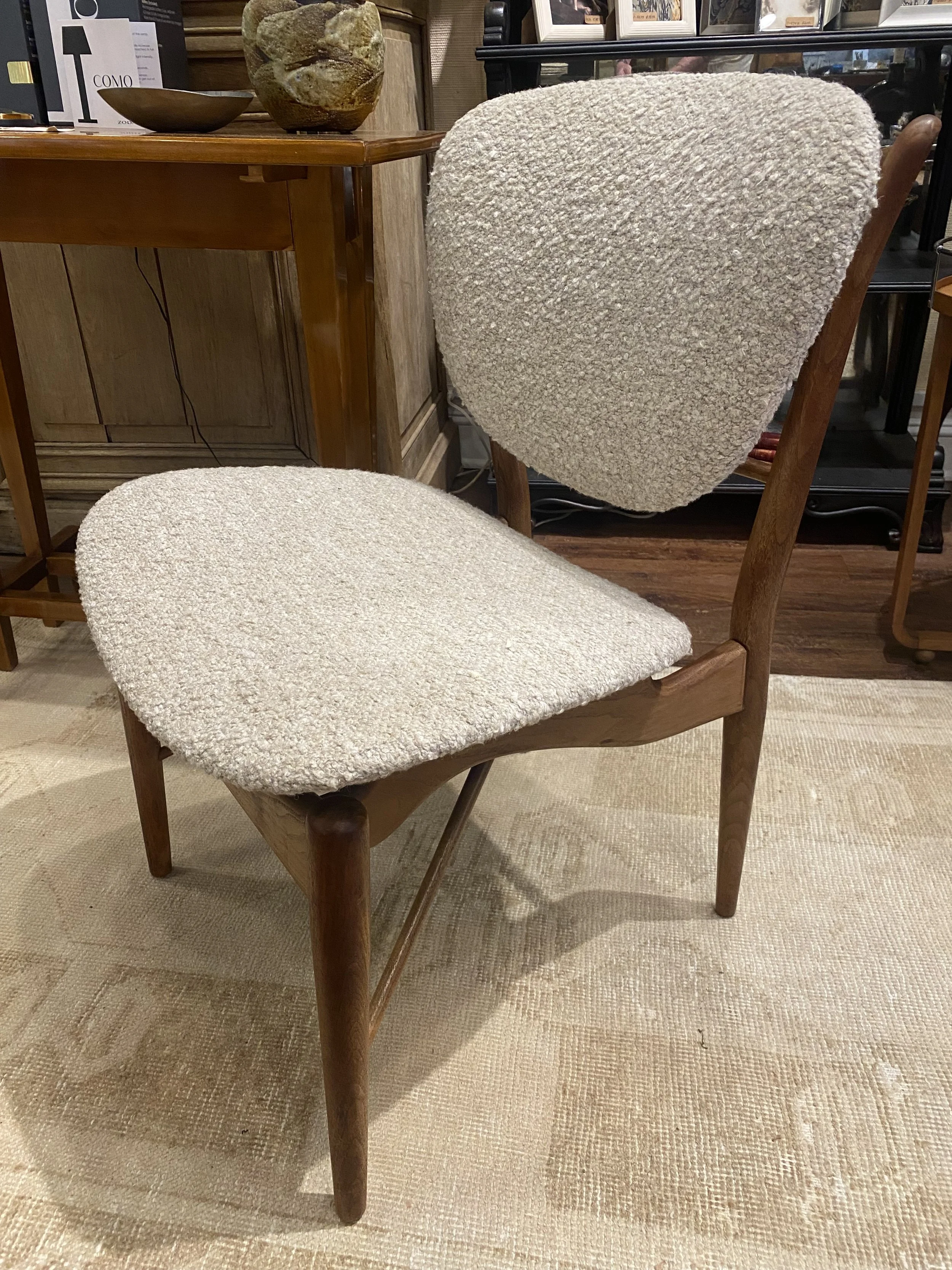 A chair with a wooden frame and a beige, textured, upholstered seat and backrest, placed on a beige rug in a furniture store.