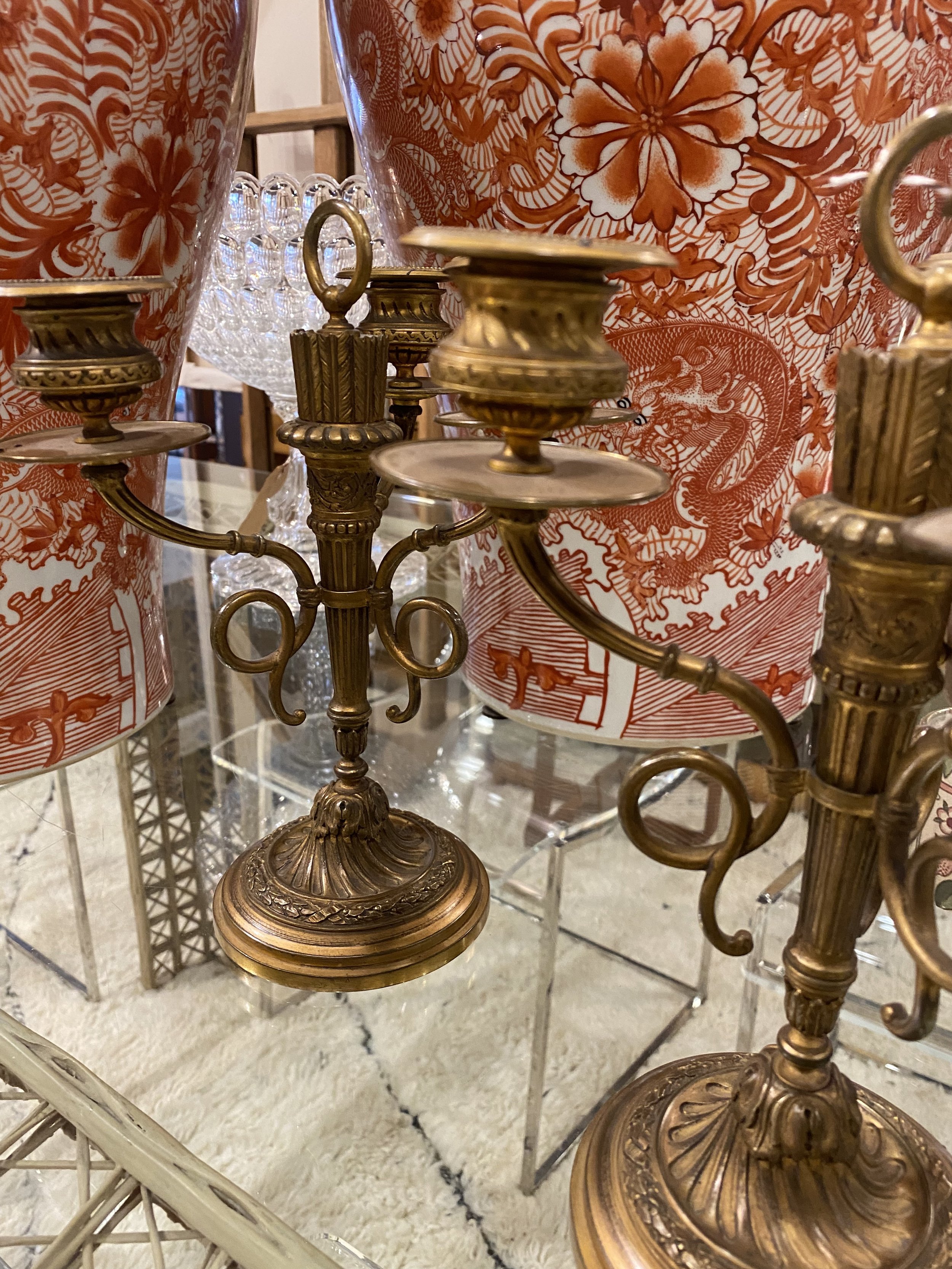 Close-up of ornate vintage brass candelabras and decorative ceramic vases with floral patterns, displayed on a glass surface with a textured rug underneath.