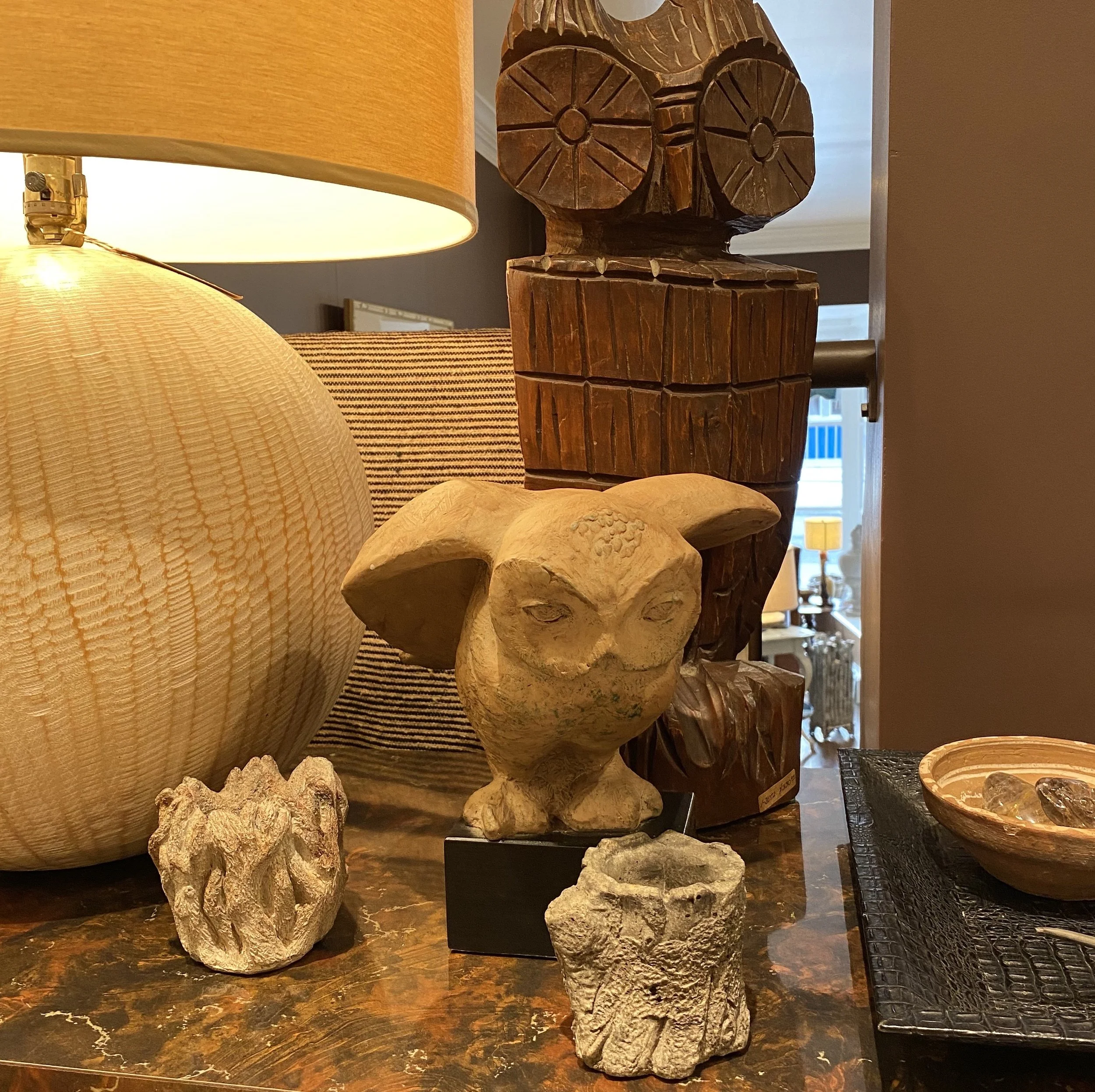 A collection of carved wooden sculptures and rocks on a dark marble surface with a warm-colored lampshade in the background.
