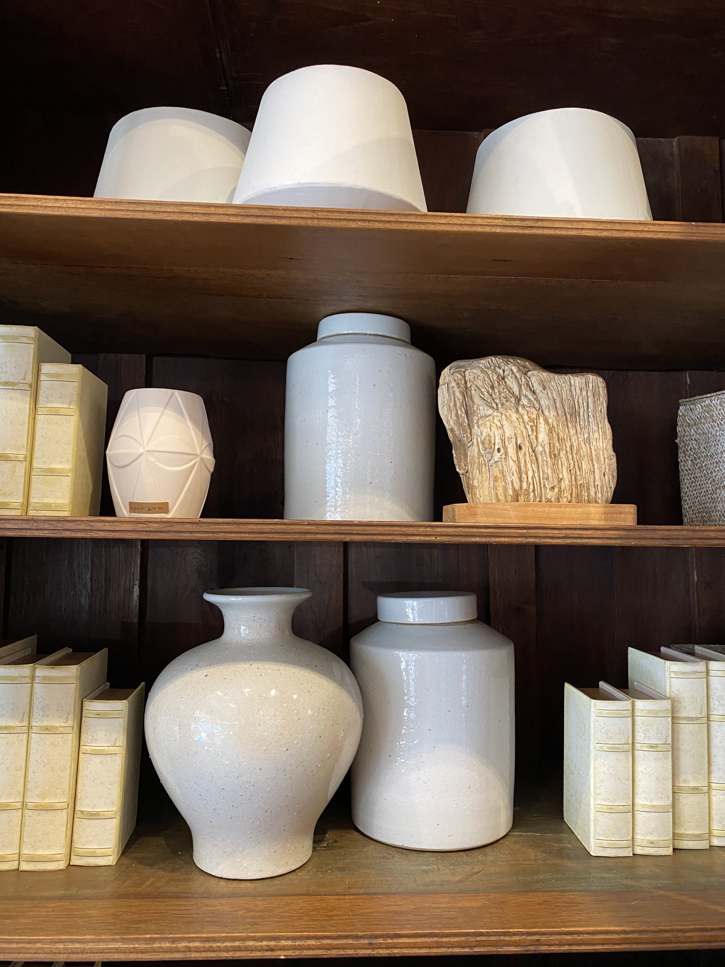 Display shelf with various decorative vases and white boxes on a wooden shelf.