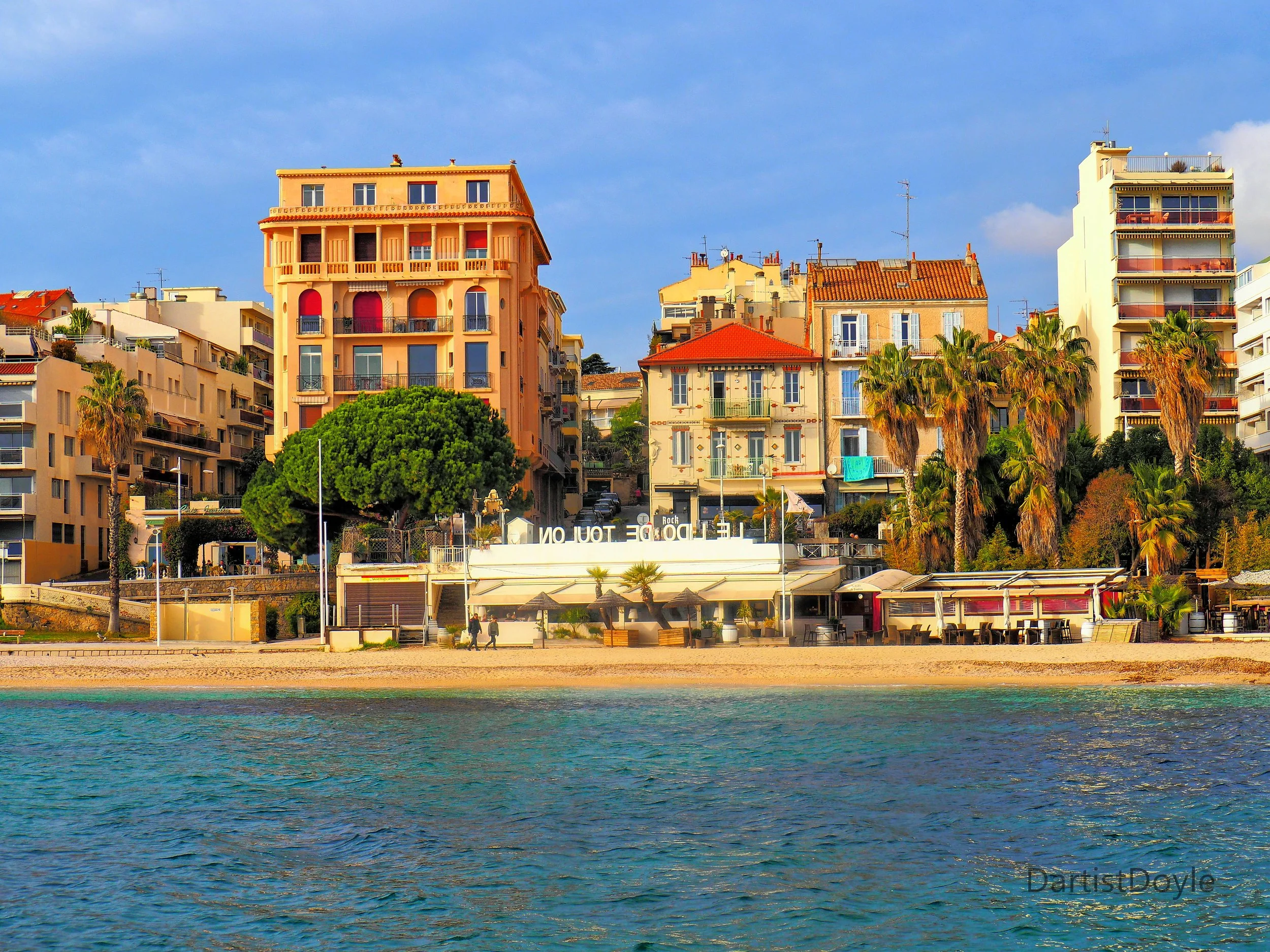 Colorful buildings along a beachfront with palm trees and a clear blue sky.