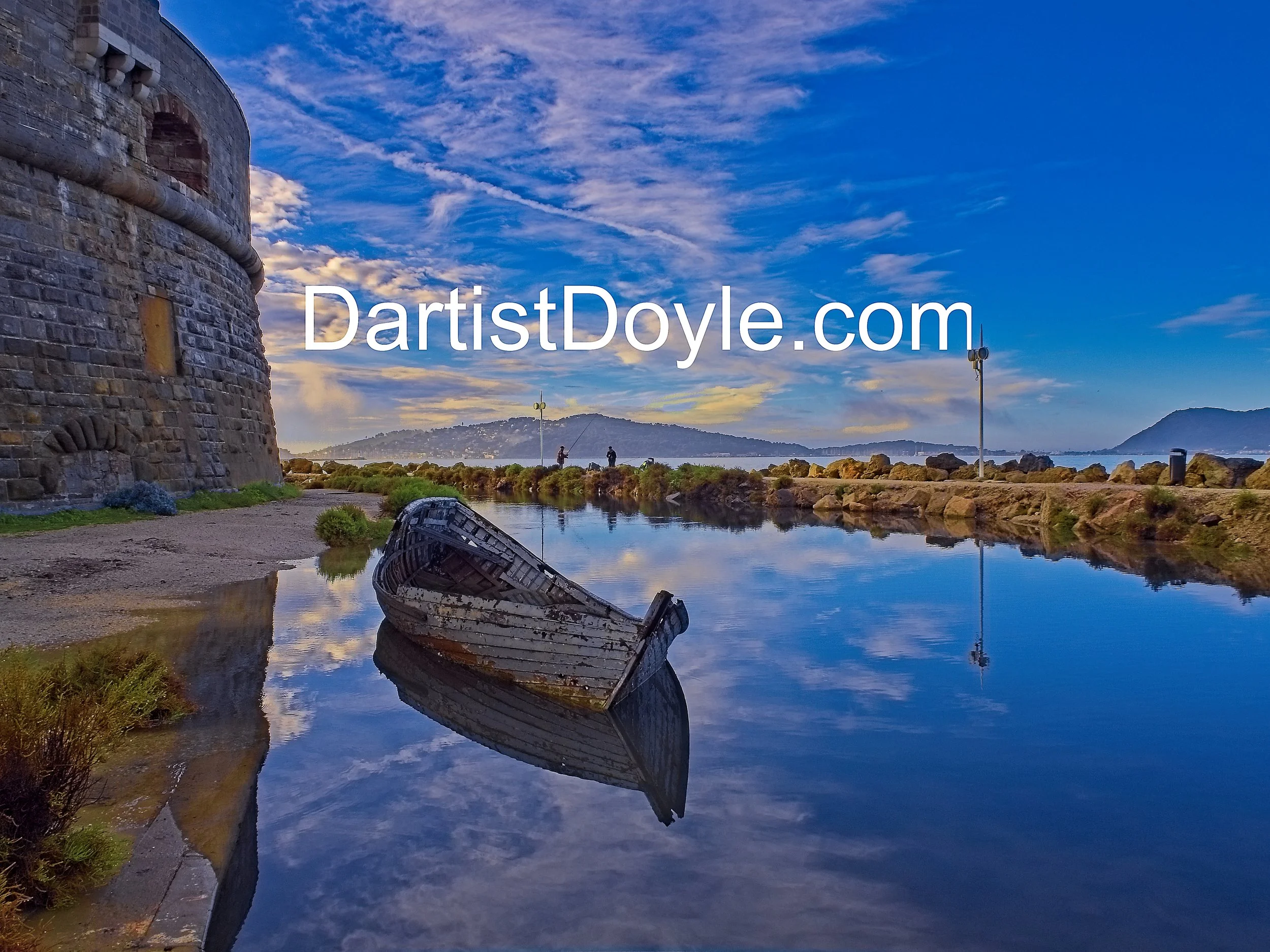 Old stone tower by a waterfront with rocks, a boat partially submerged in the water, and a sky with scattered clouds.