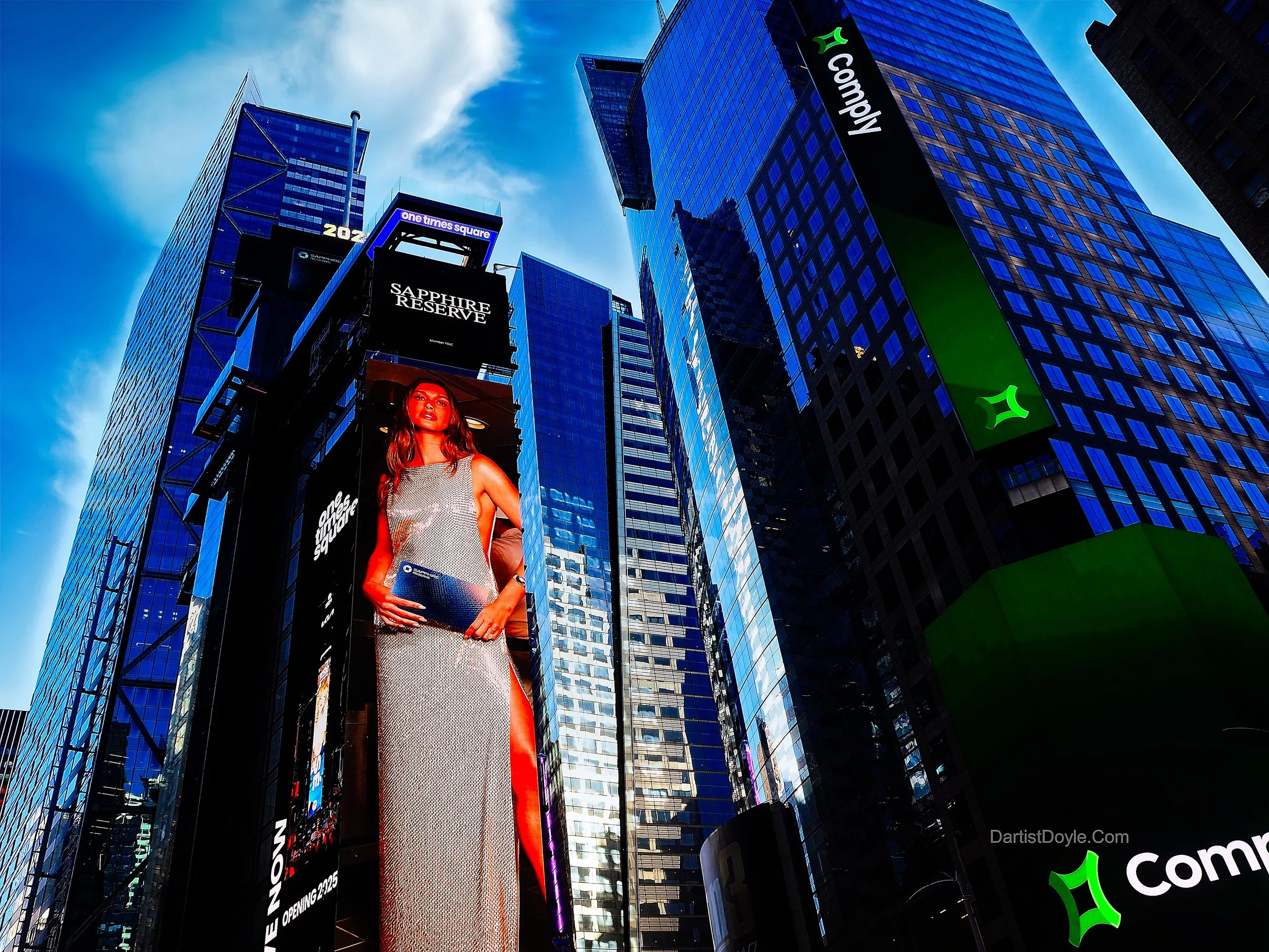 Tall modern skyscrapers with reflective glass windows in Times Square, New York City, featuring electronic billboards including an advertisement of a woman in a dress and the Sapphire Reserve logo.