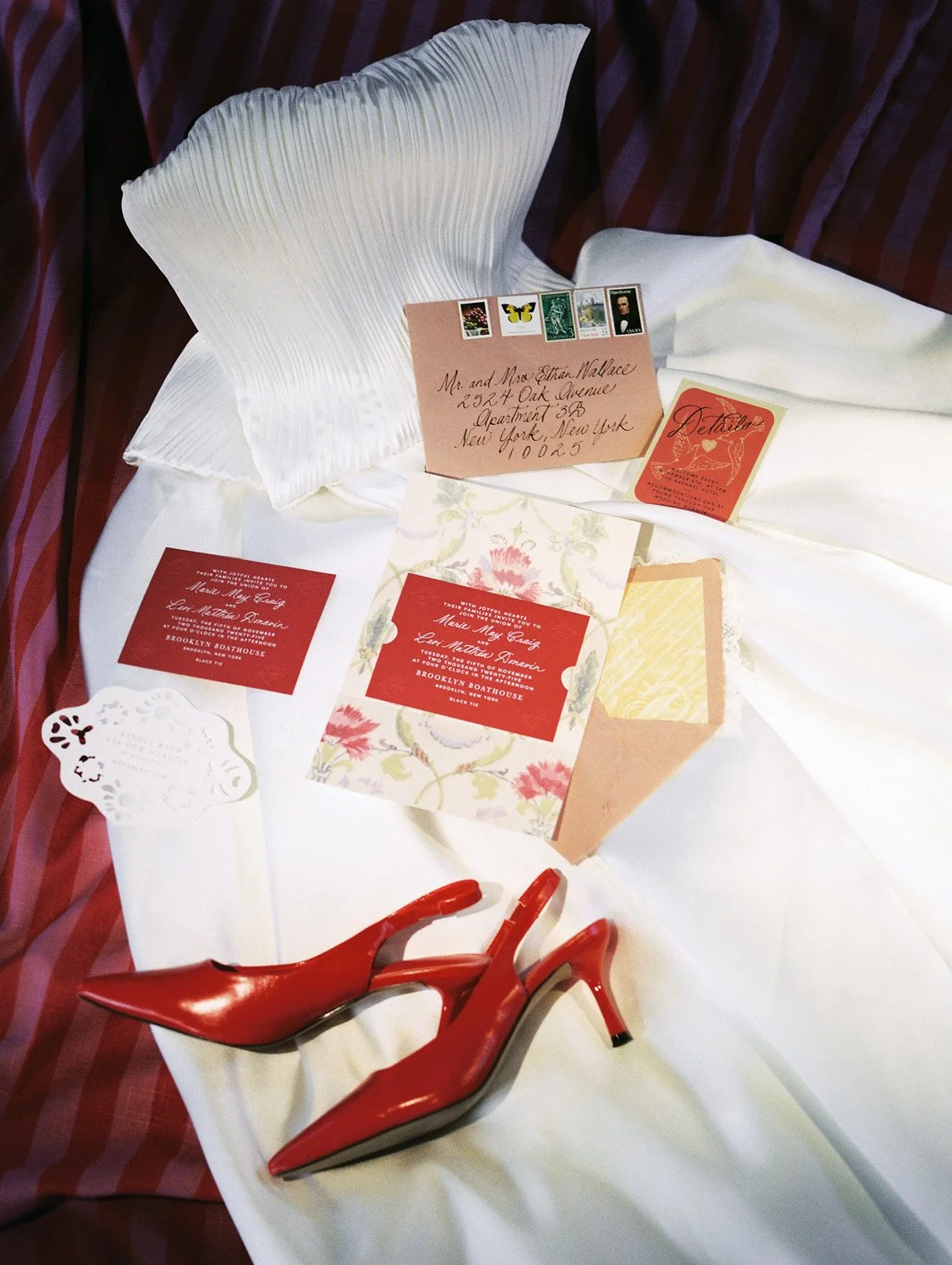 Wedding invitations, envelope, and red high-heeled shoes on a white tablecloth.
