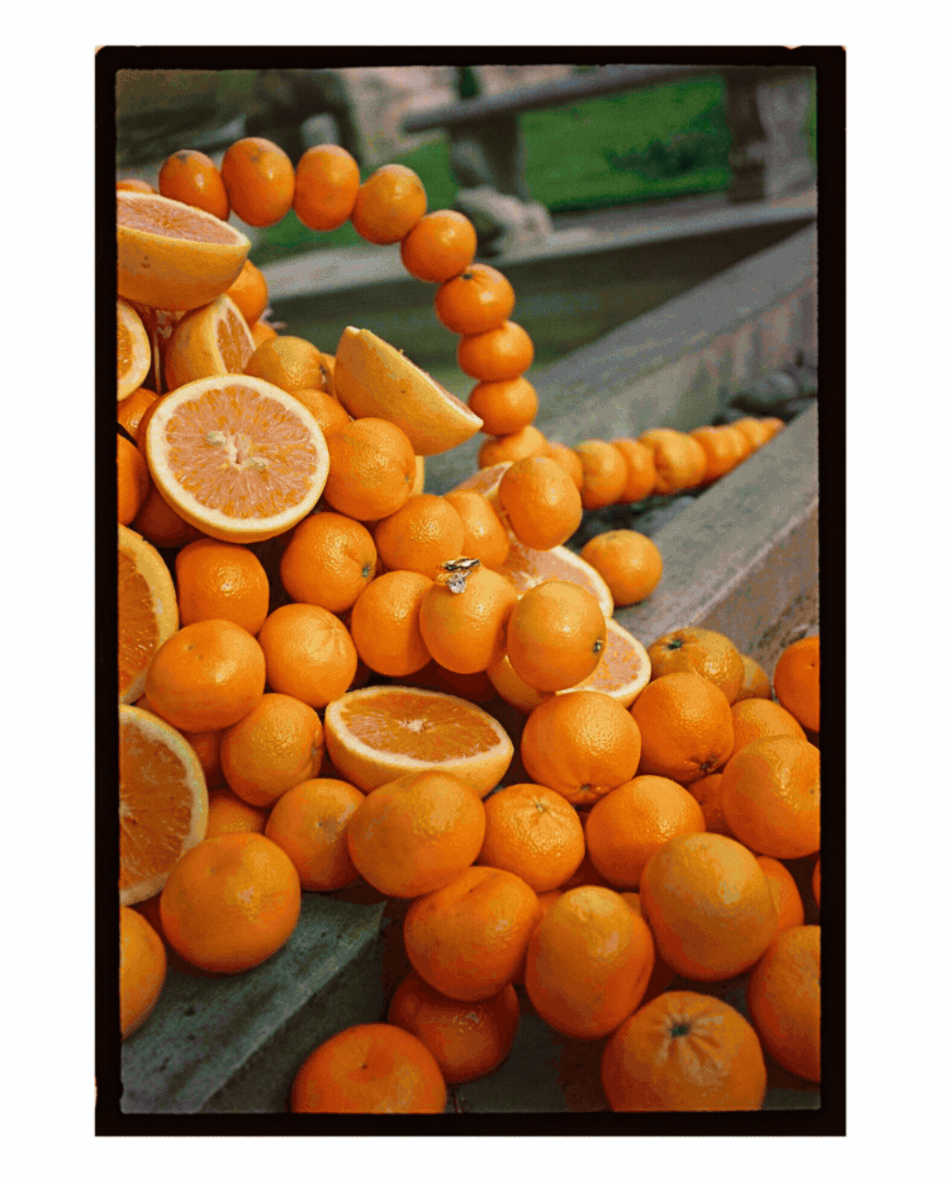 A pile of oranges, some cut in half, arranged on a wooden surface outdoors.