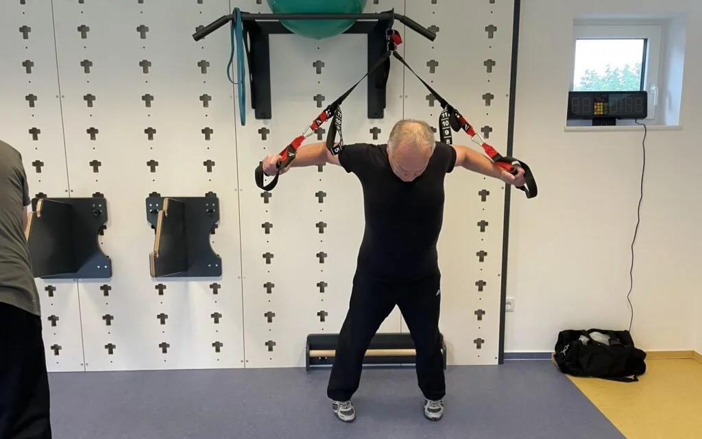Älterer Mann trainiert mit einem Suspensio­strainingsträger in einem Fitnessraum.