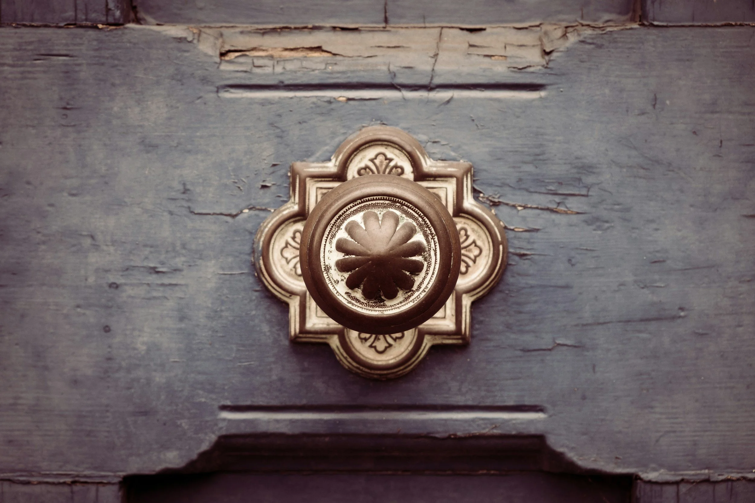 A high-contrast architectural close-up of an ornate metallic door knob on a weathered door, illustrating detail-oriented precision, security, and an exclusive gateway to operational clarity.