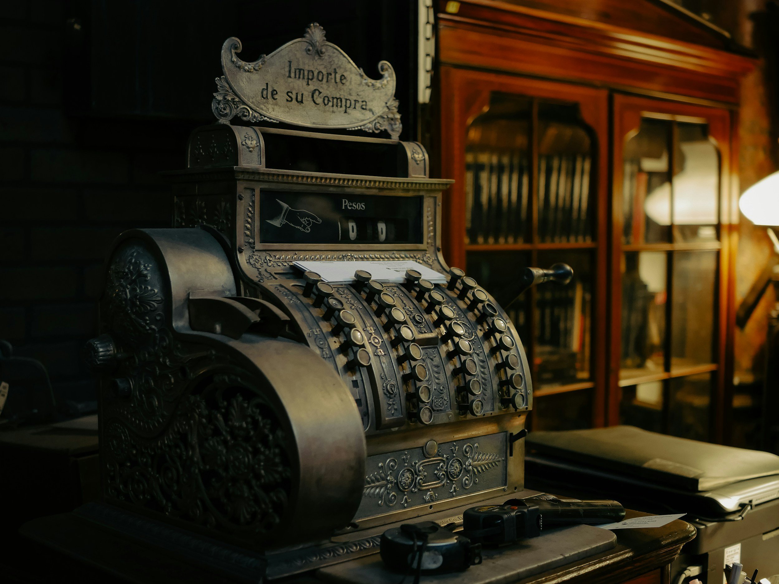 An ornate vintage cash register resting next to a dark wood bookshelf, symbolizing classic business heritage, financial legacy, and meticulous ledger tracking for specialized professionals.
