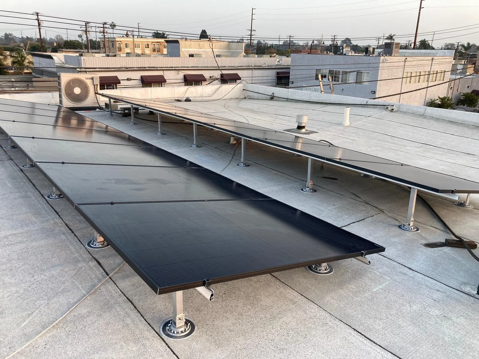 Solar panels installed on a building rooftop with visible piping, vents, and an air conditioning unit, under a cloudy sky.