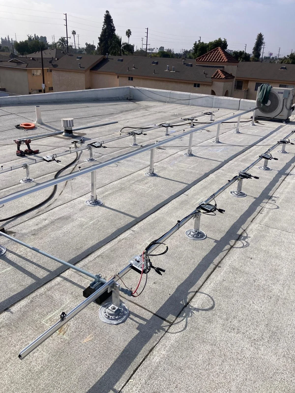 Rooftop with mounting brackets and solar panel wiring, air conditioning unit, and a vent pipe on a commercial building.