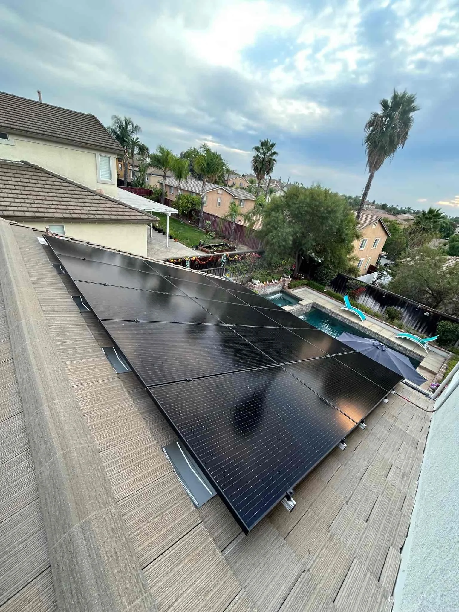 Backyard with solar panels on the roof and a swimming pool with lounge chairs and an umbrella