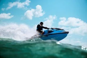 Person riding a blue jet ski on the water with a blue sky and clouds in the background.