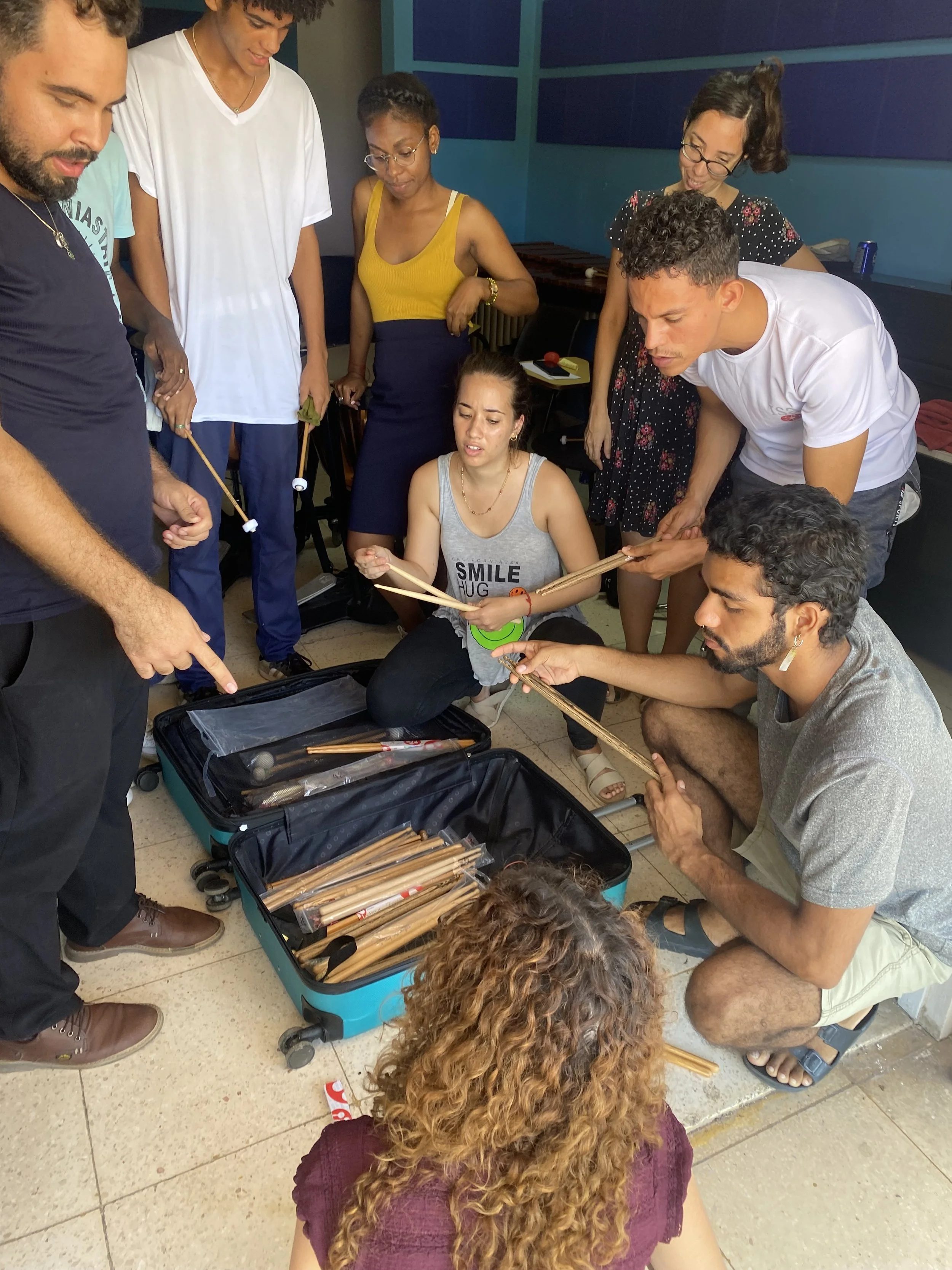Group of people gathered around an open suitcase with sparkling sticks, some holding the sticks, others looking at the contents inside.