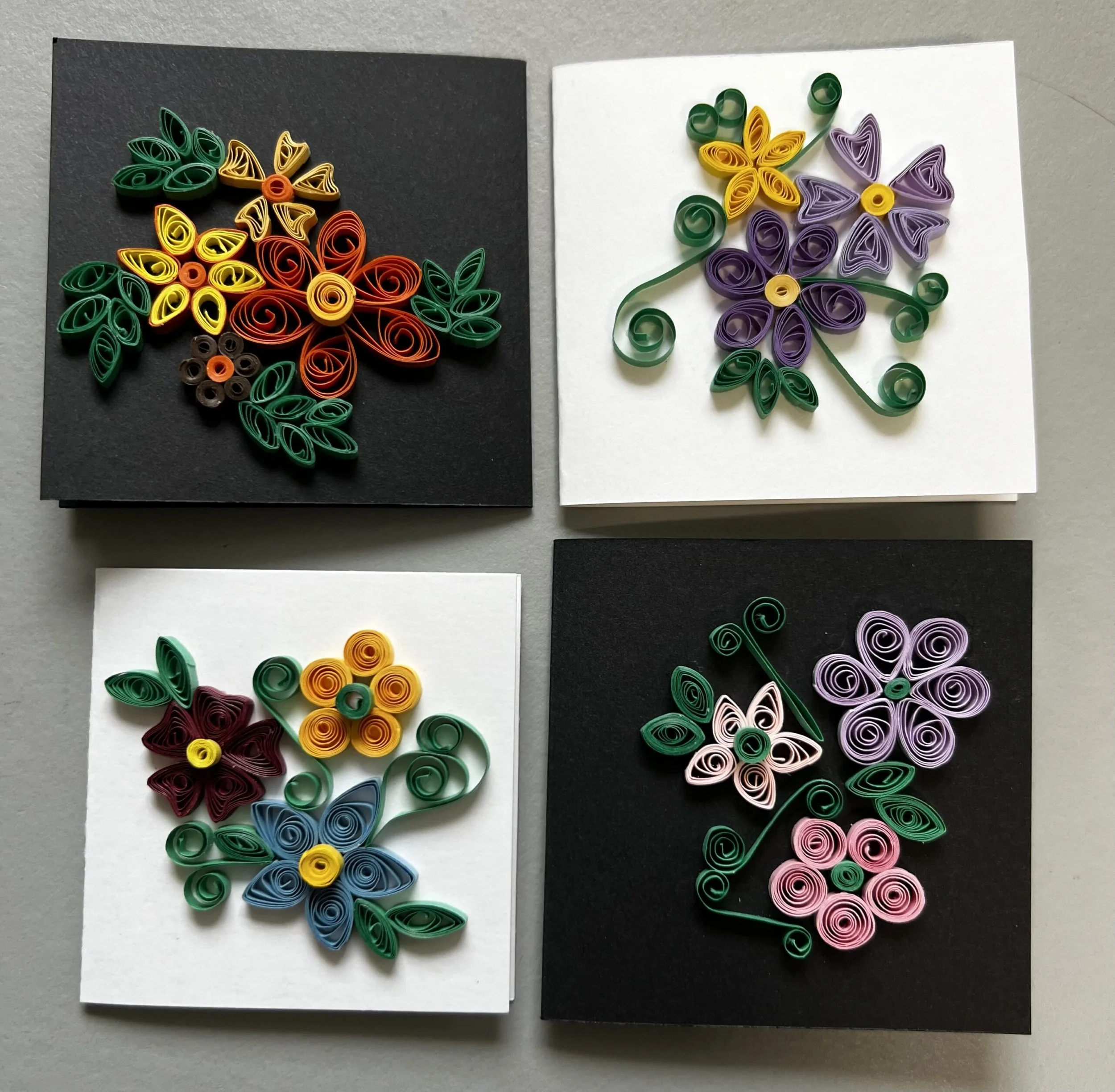 Four pieces of paper with colorful quilled paper flowers on dark and white backgrounds.