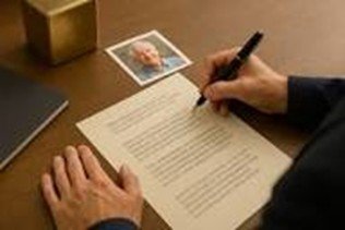 Person signing a document at a desk with a photograph and a small box nearby.
