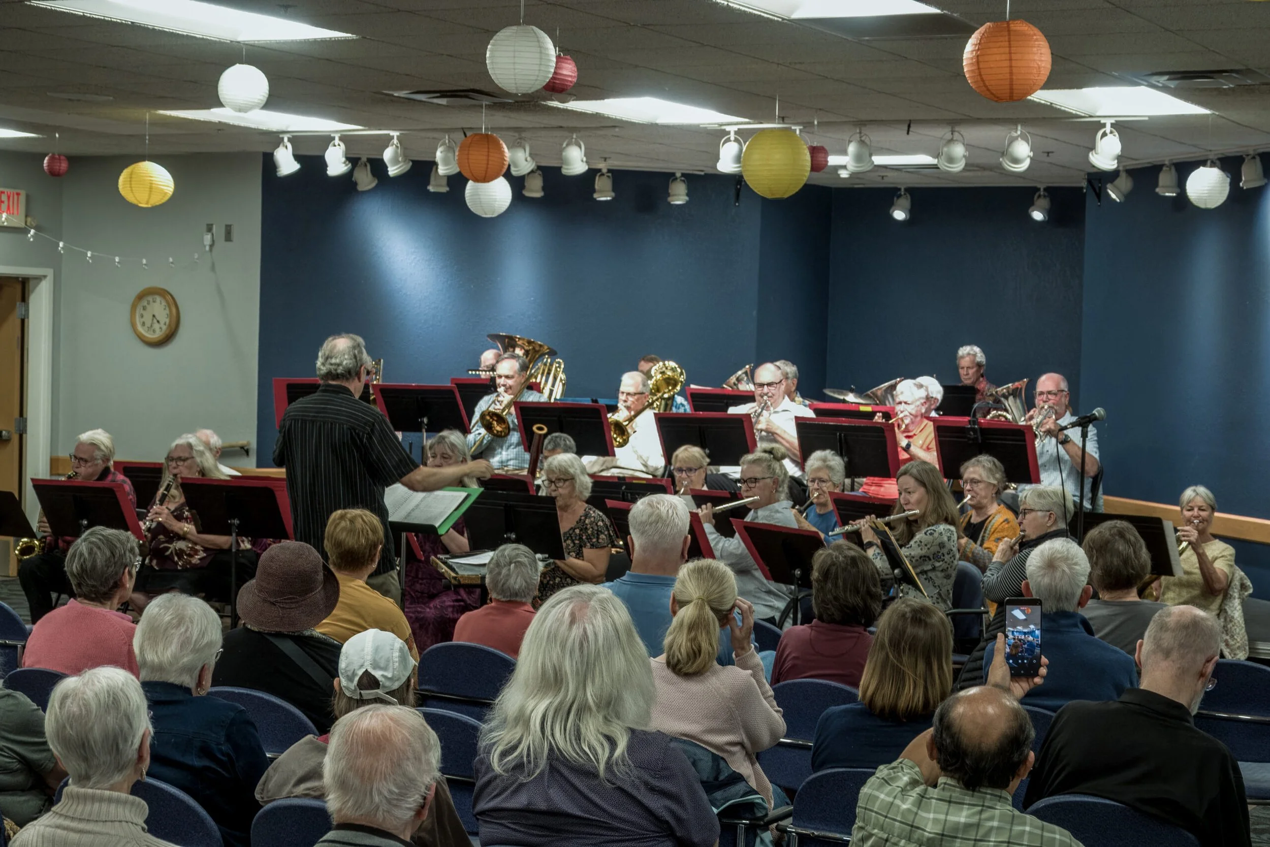 An orchestra performing in a room filled with an audience of mostly older adults.
