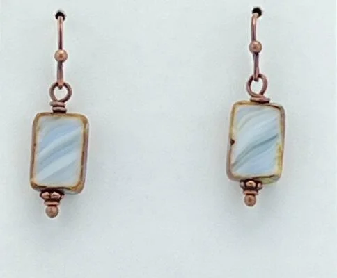 A pair of earrings made of rectangular stones with a light blue marbled appearance, set in copper-colored metal with loop and bead details.